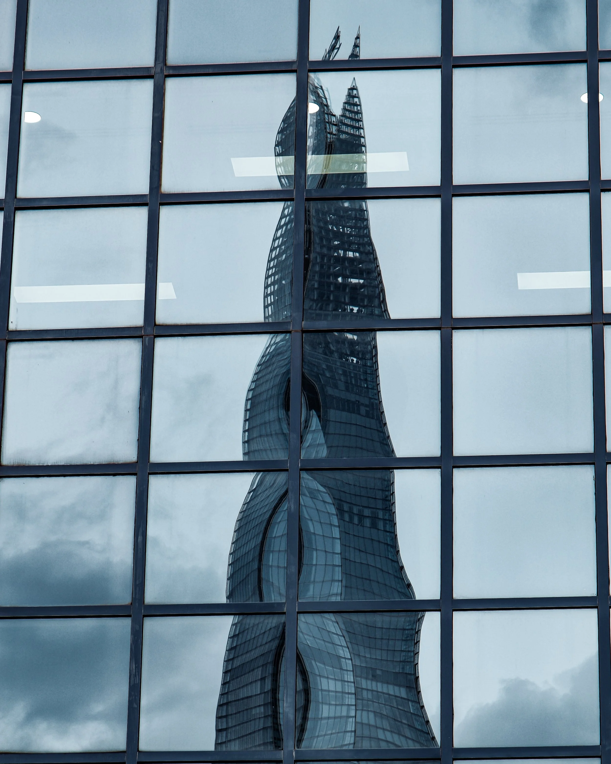 Reflection of a modern, glass skyscraper with curved design in the windows of a neighboring building.