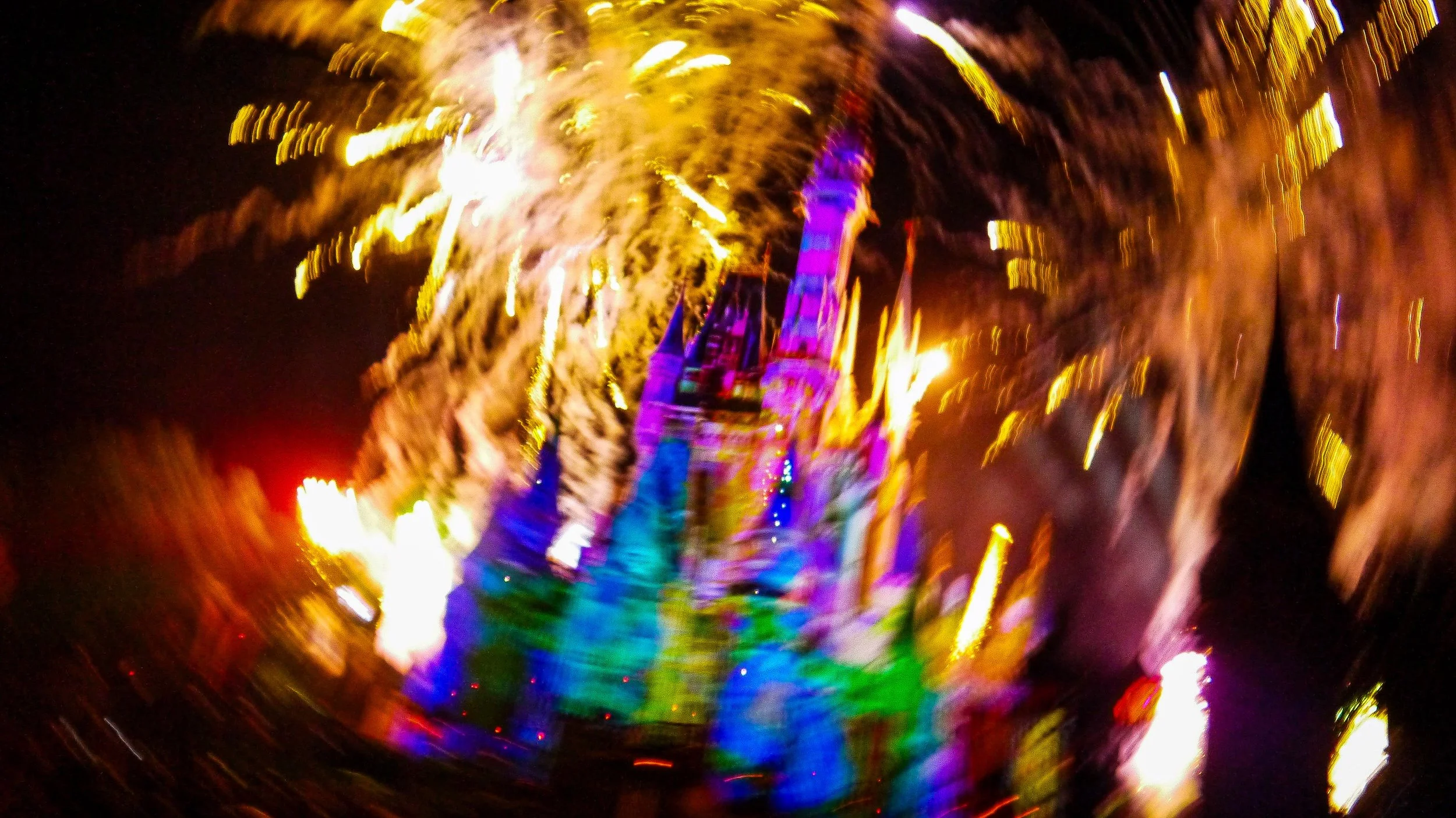 Blurred colorful lights creating a swirling effect with a silhouette of a tower or structure at the center during nighttime.