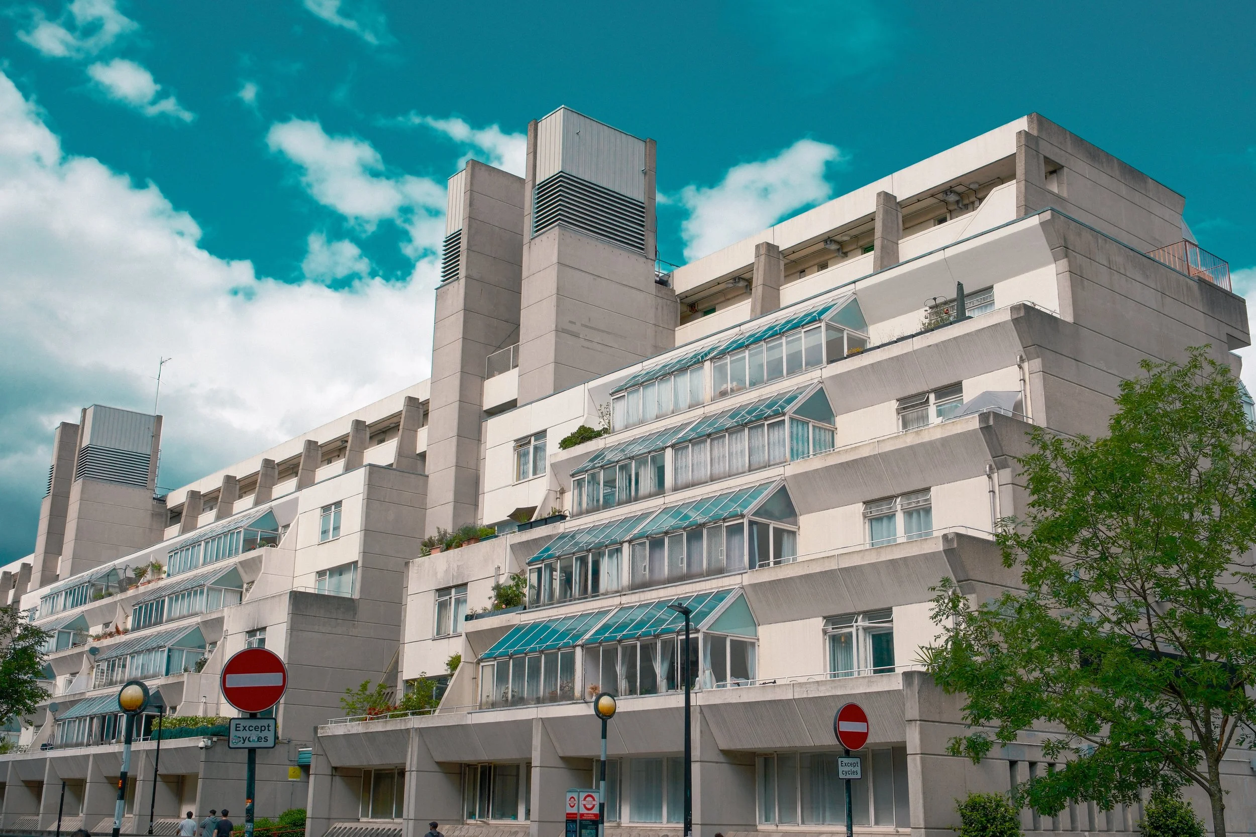 A multi-story residential building with many balconies and large windows, topped with a blue sky and some clouds.