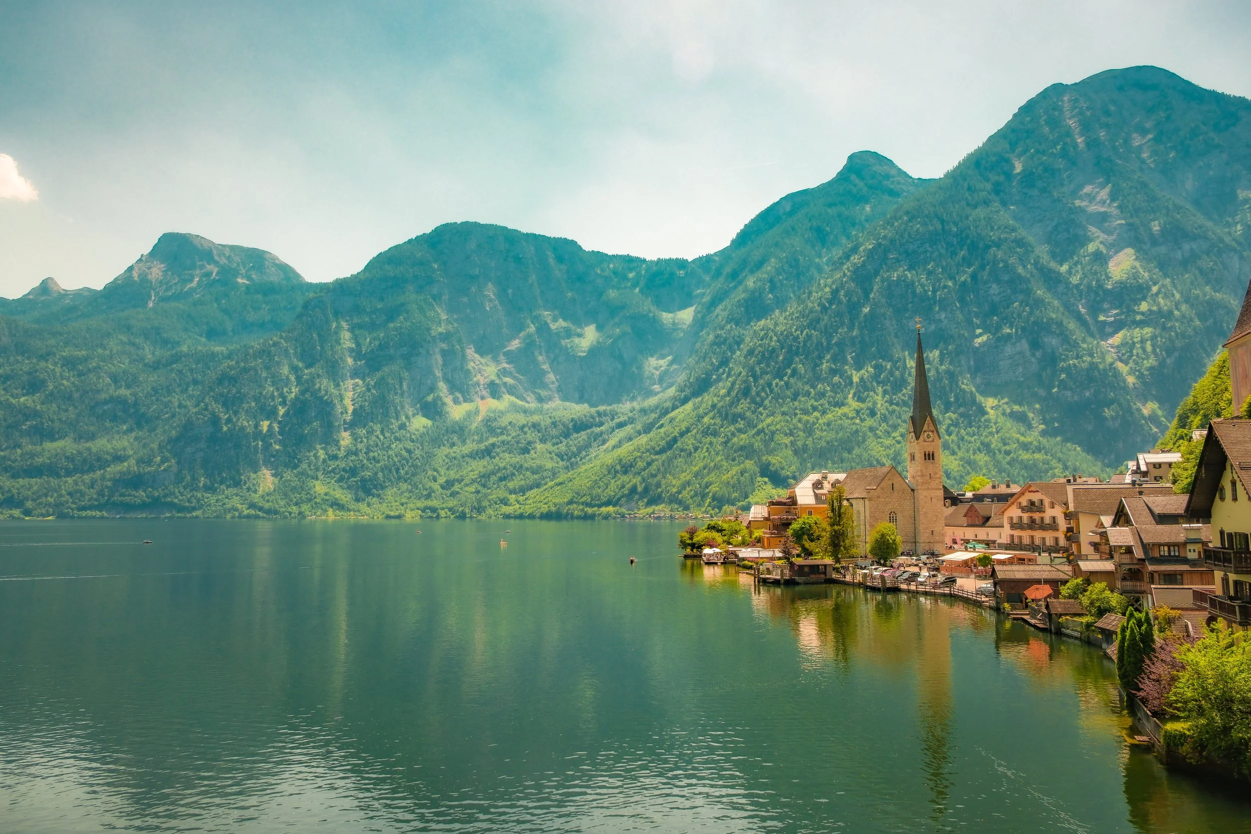 A lake with surrounding mountains and a small village with buildings and a church steeple in the foreground.