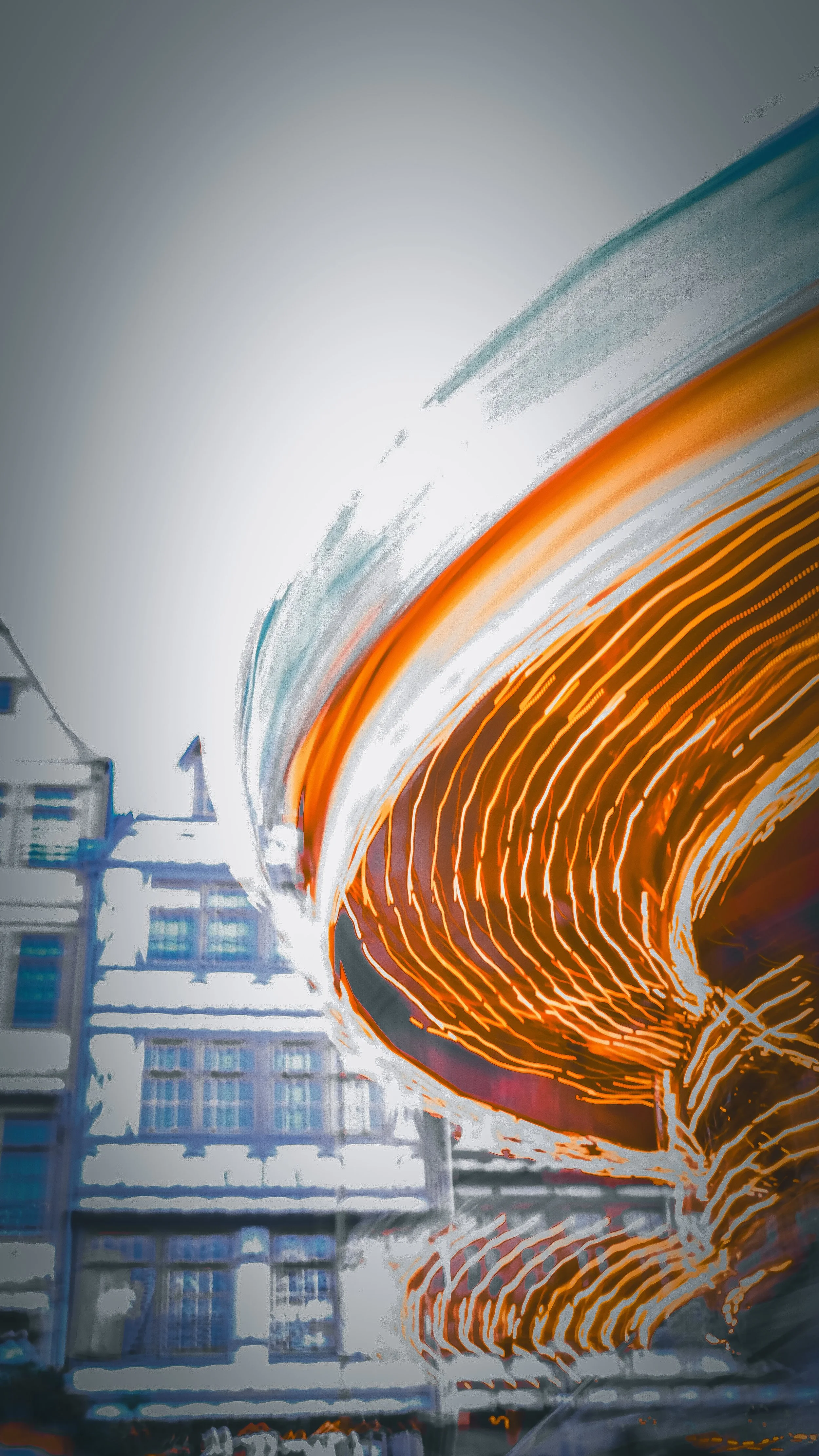 Long-exposure photo of spinning orange traffic light creating concentric light trails with buildings and clouds in the background.