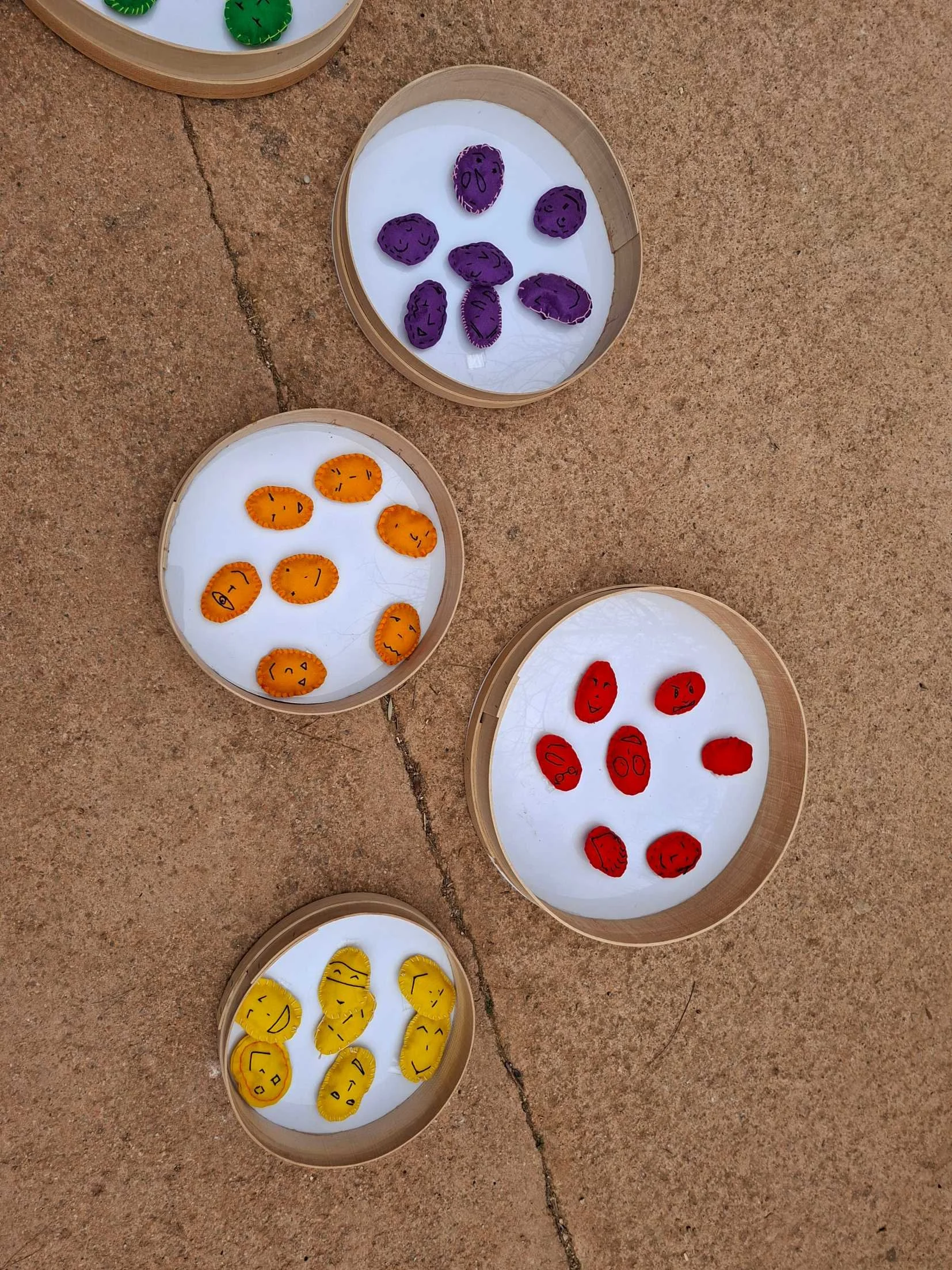 Colorful felt rocks with faces drawn on them, arranged in baskets on the ground.