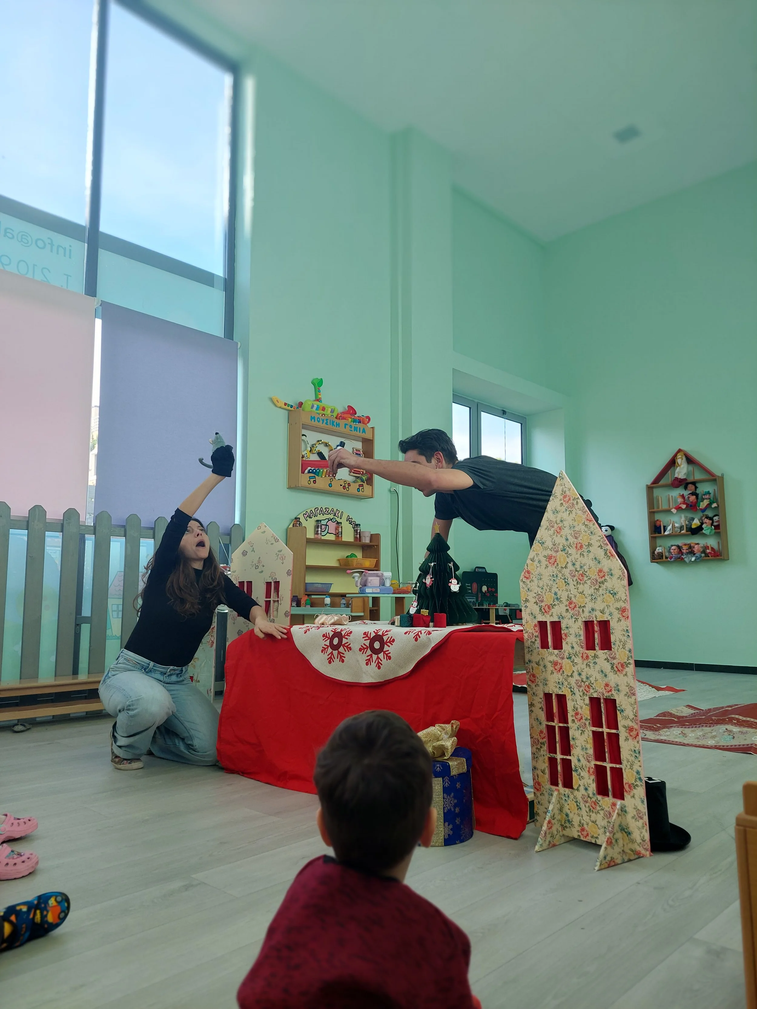 Children and adults participating in a puppet show or theater performance with holiday decorations in a playroom.