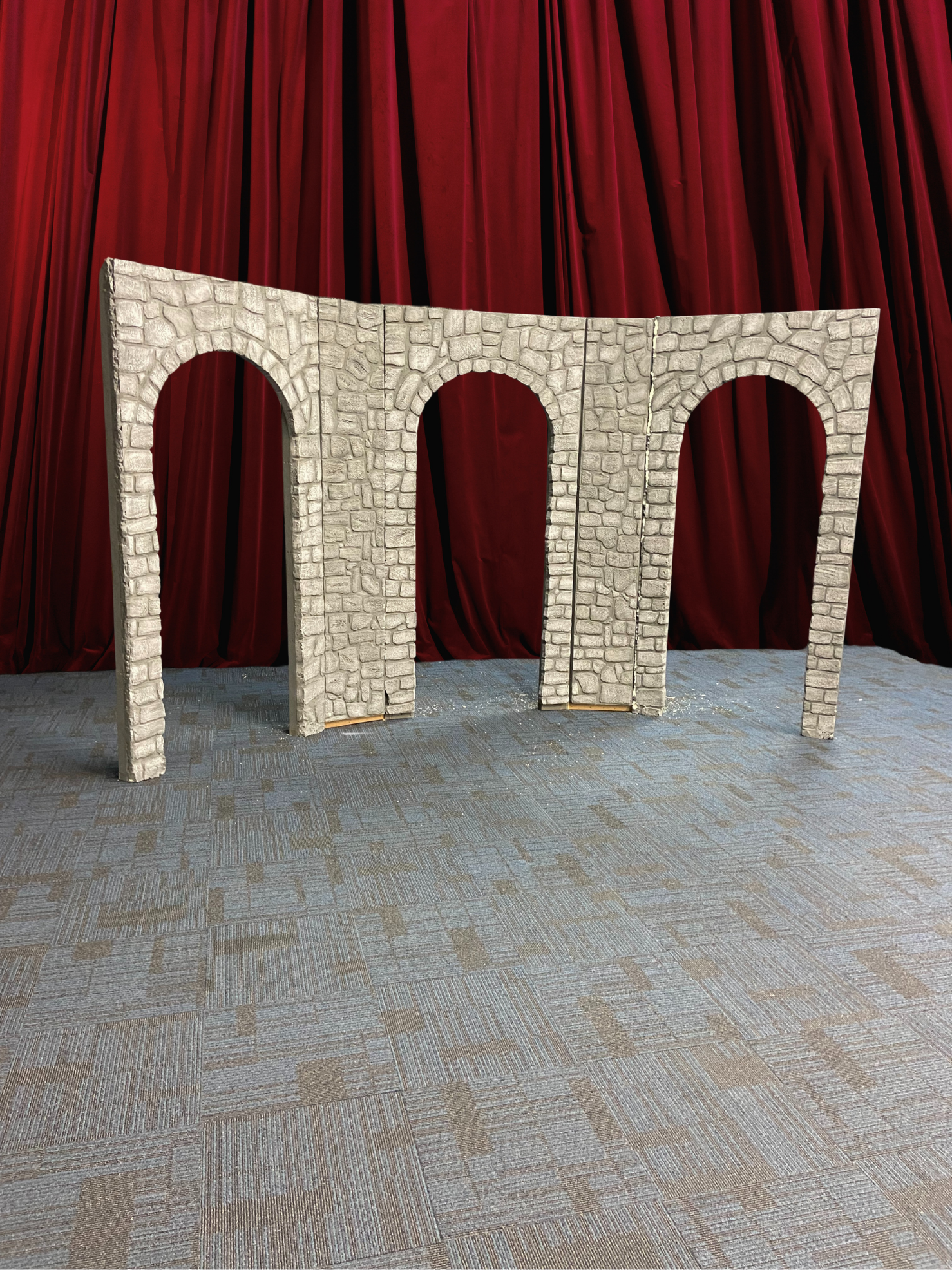A structure resembling three stone arches standing on a carpeted stage with red curtains as the backdrop.