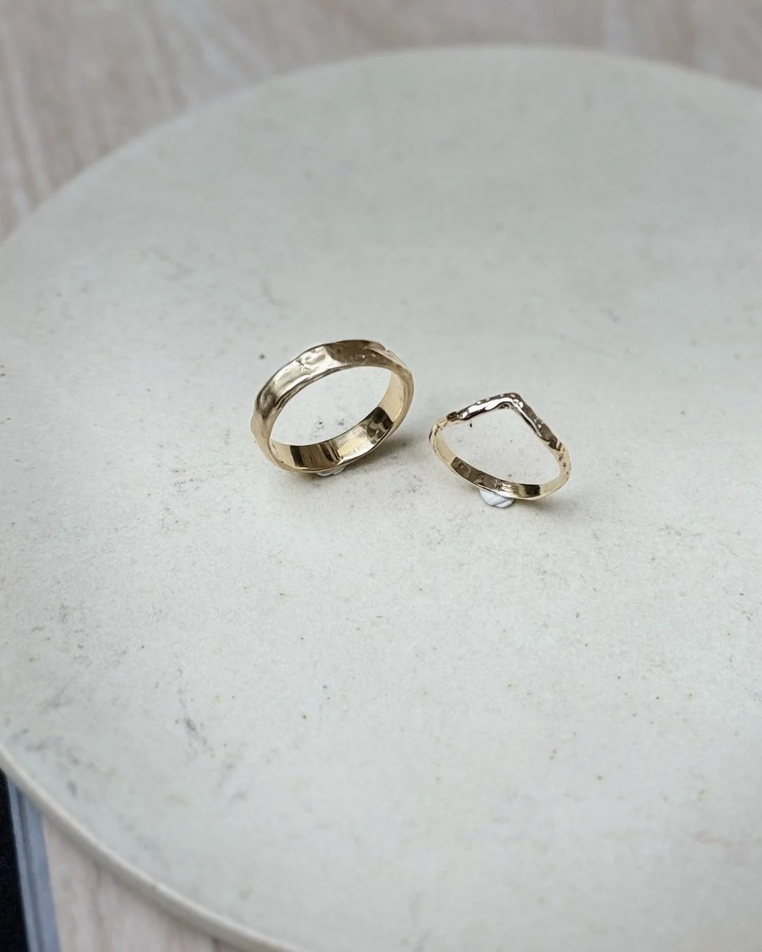 Two handmade 14ct gold wedding rings, one larger and one smaller, placed on a white textured surface.