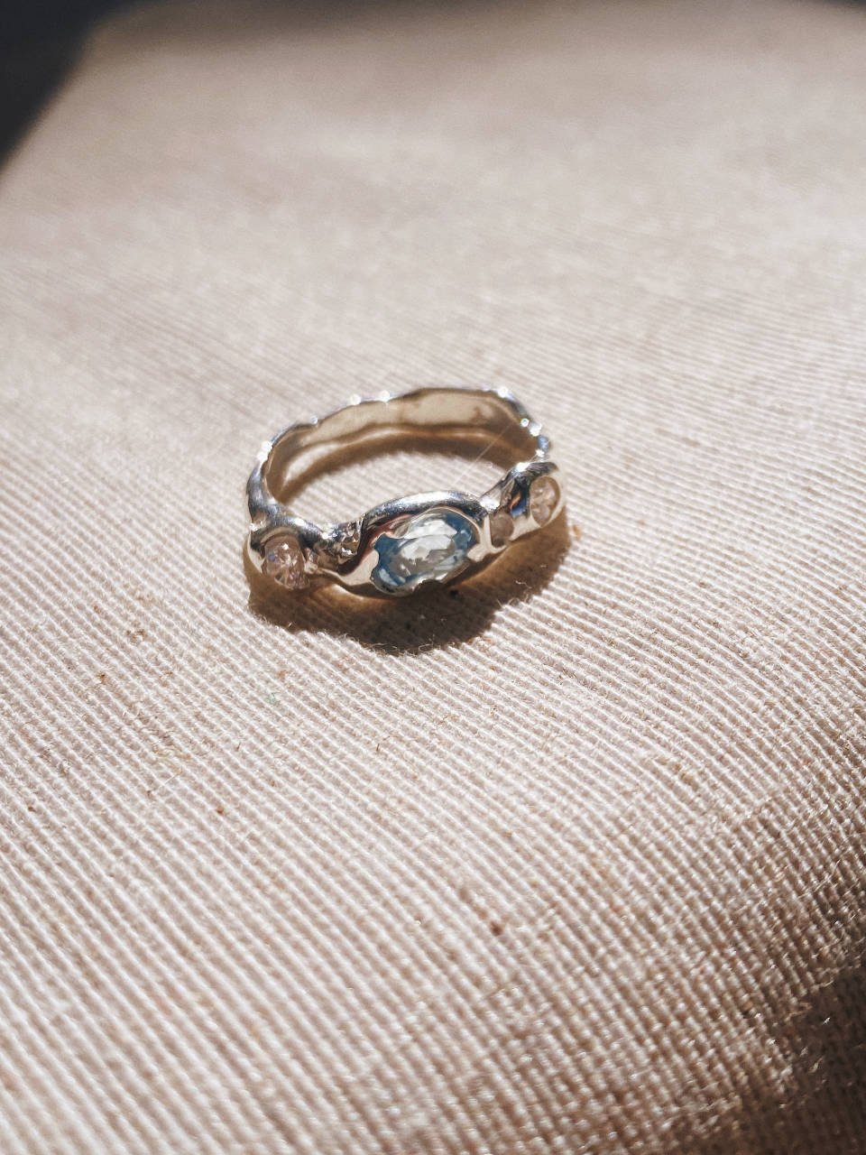 Unique handmade ring with light blue topaz and two diamonds, designed with a raw sculptural look and timeless modern style.