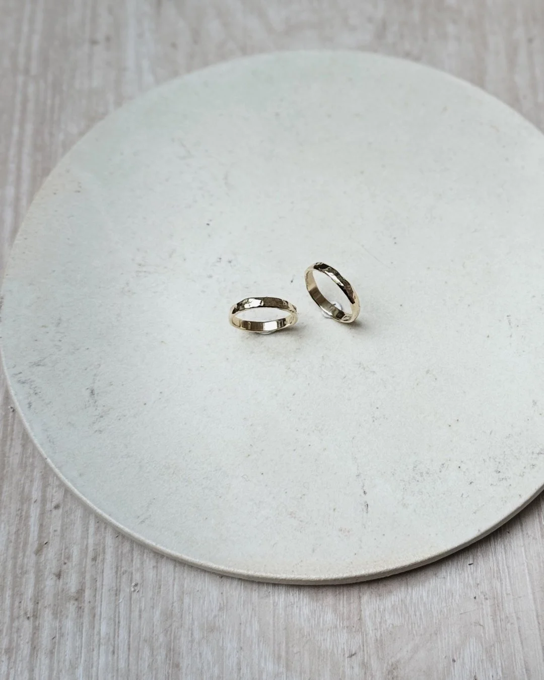 Two gold wedding rings on a white round surface with a grey wooden background.