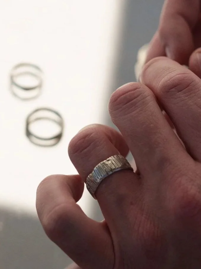 Modern men’s ring in recycled 14ct or 18ct gold or sterling silver, featuring a wide band, asymmetrical edges and artisanal textured finish.