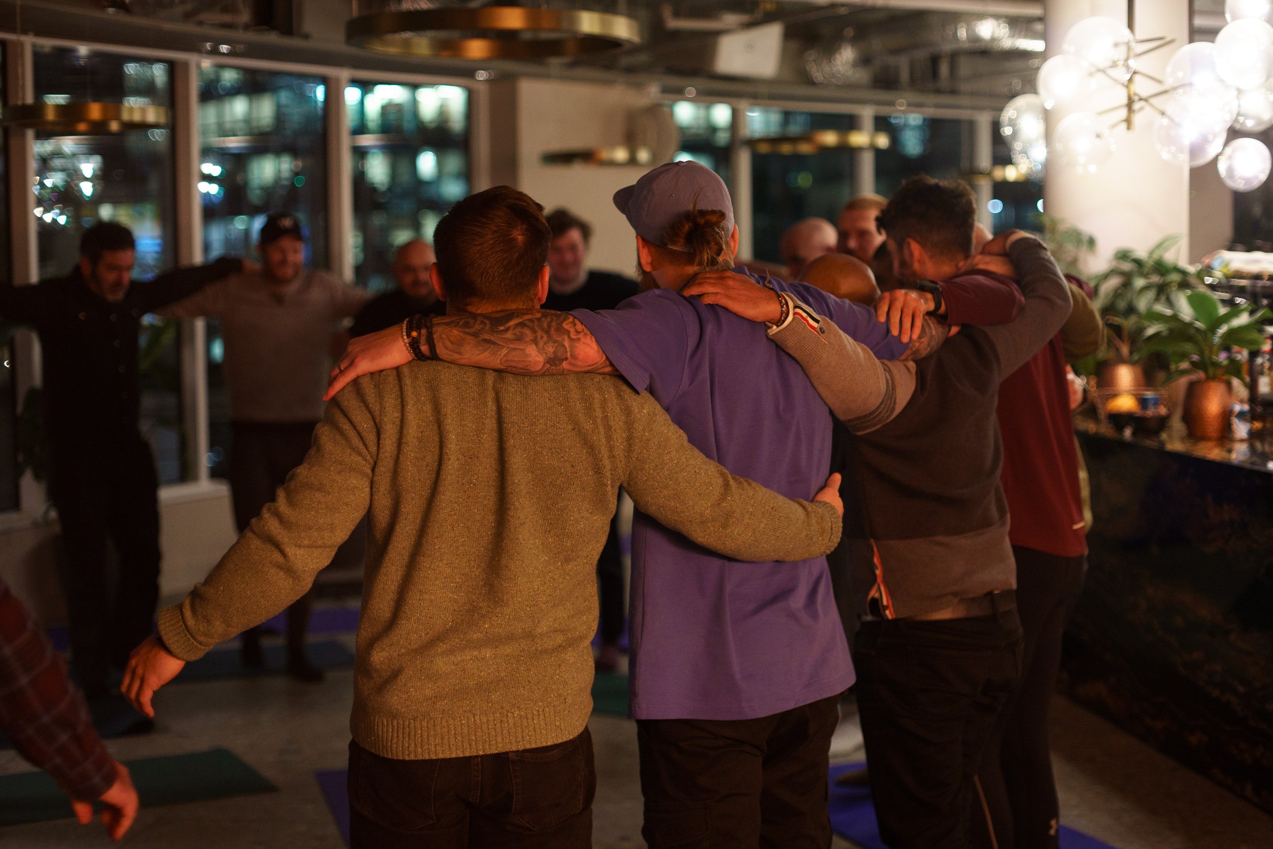 A group of people standing in a circle with their arms around each other's shoulders outdoors at night, at a breathwork event hosted by Josh Connolly.
