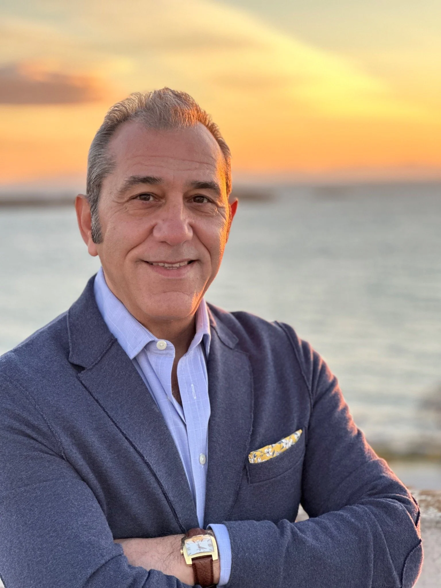 Portrait of Emad Shargi, former American hostage and keynote speaker, in a blue suit with a sunset backdrop.