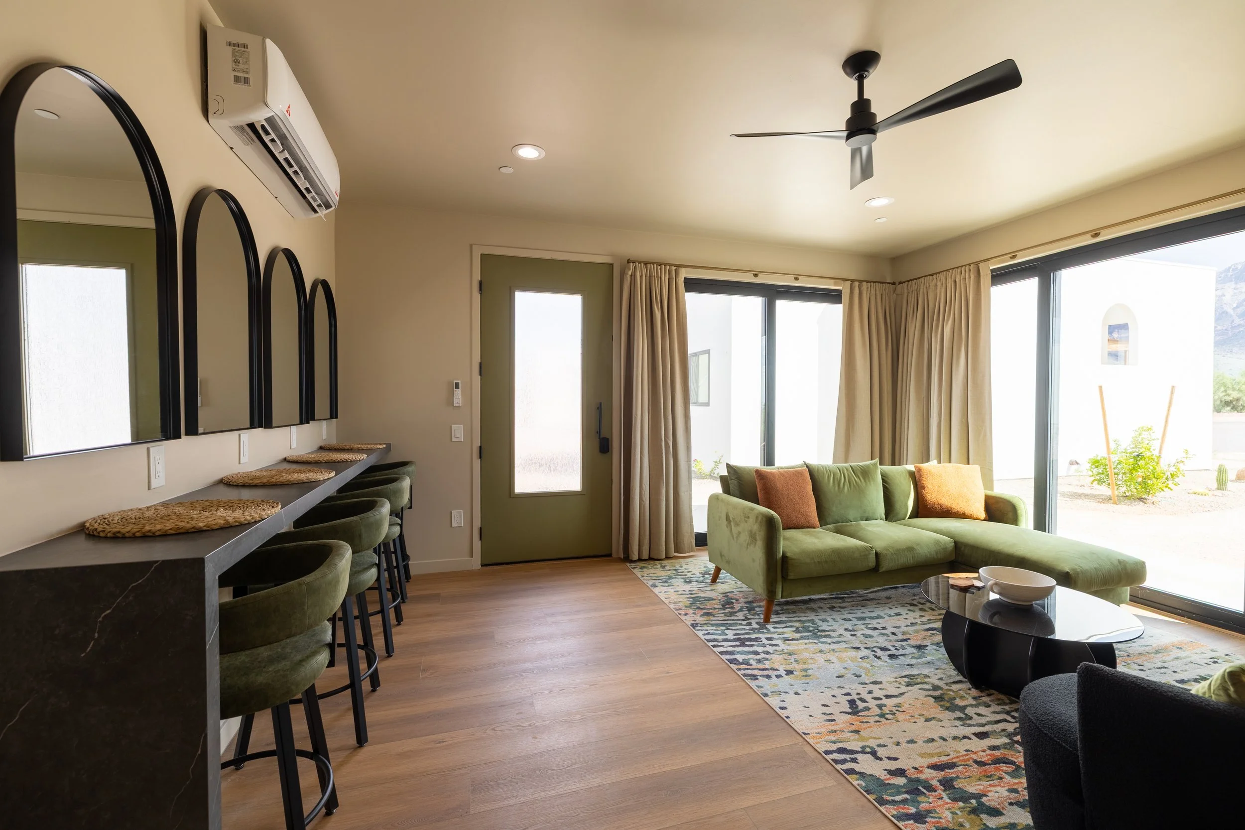 Living room with a green sofa, sliding glass doors, beige curtains, a patterned area rug, and a black coffee table.