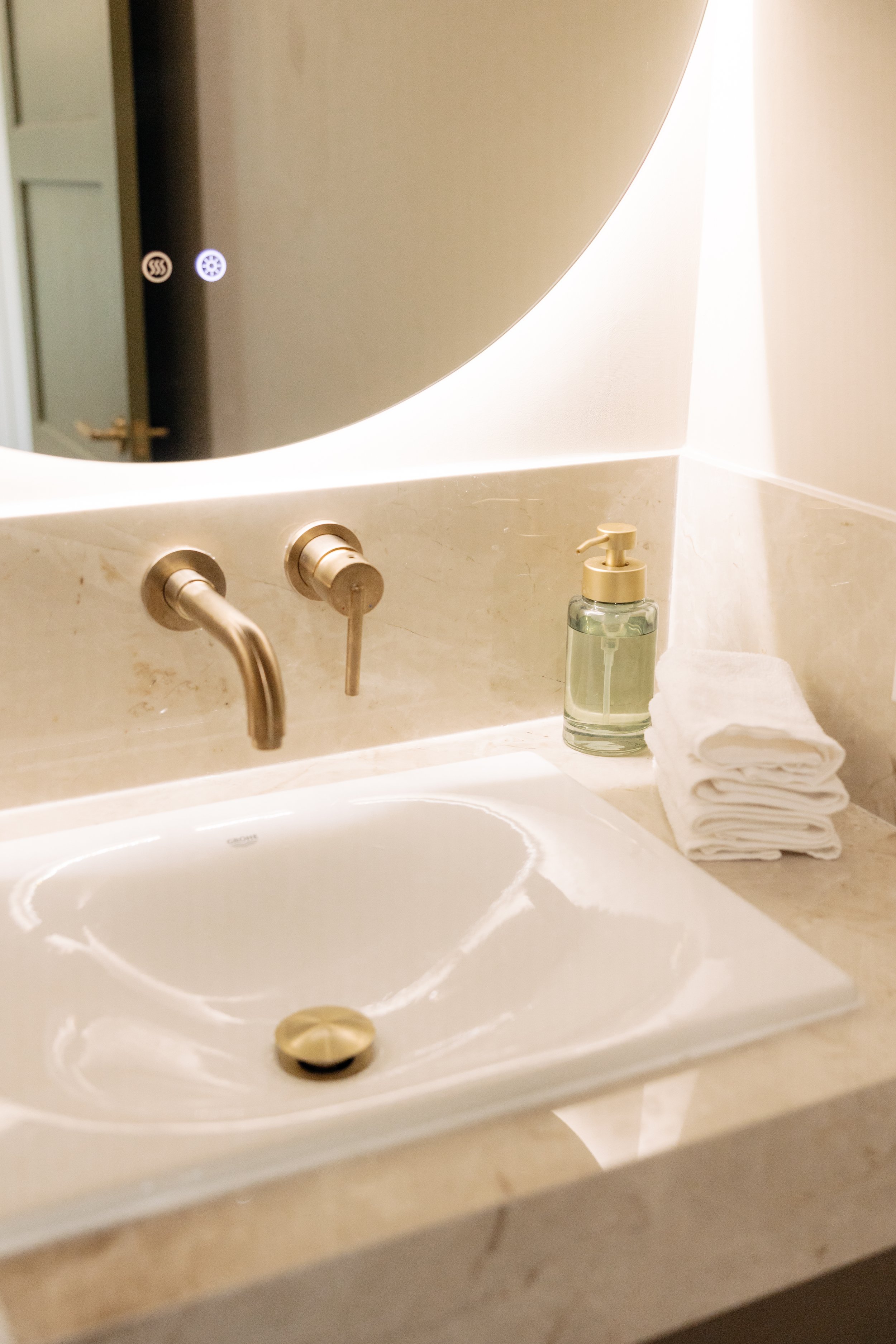 Bathroom sink with gold faucet, soap dispenser, rolled white towels, and a large mirror.