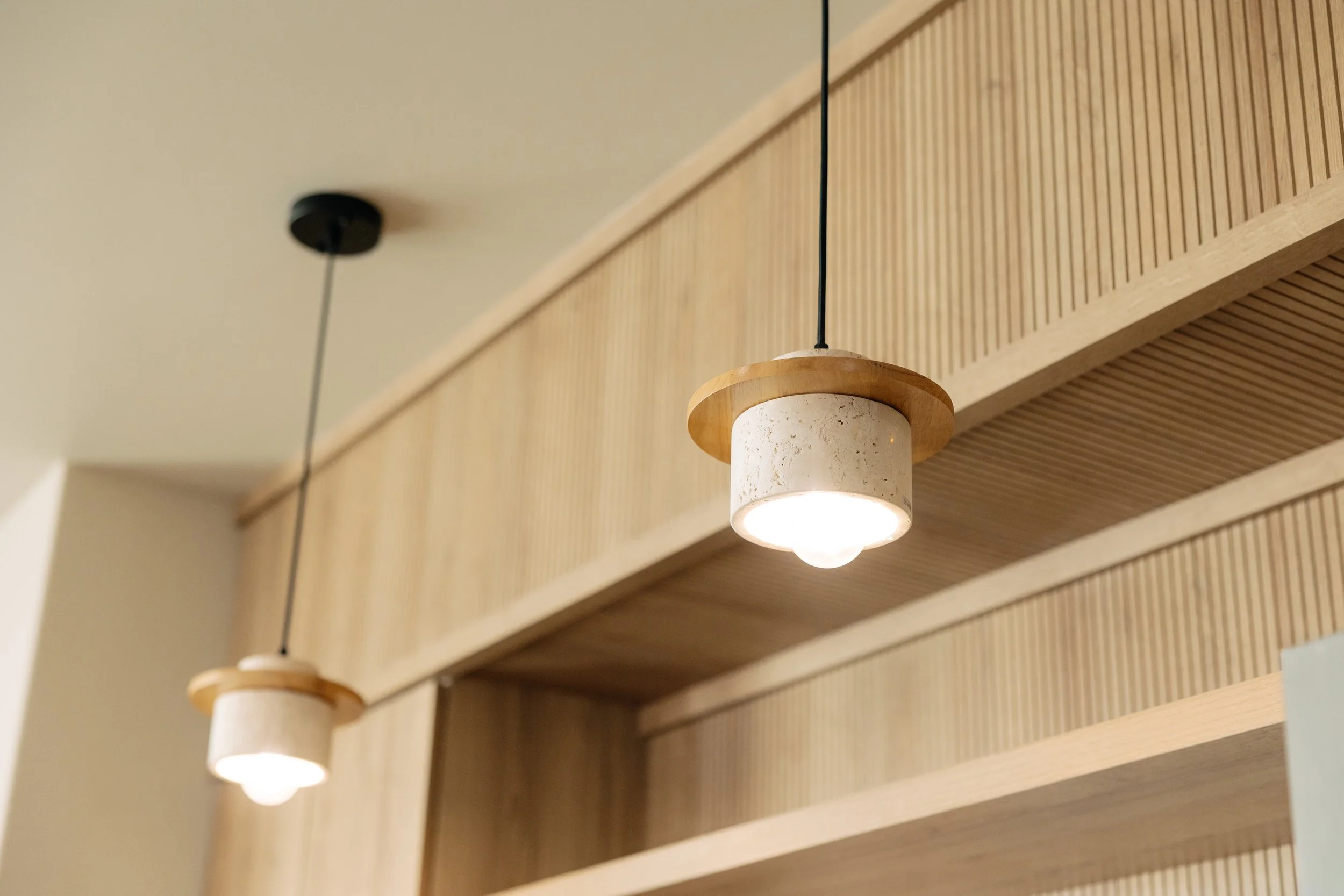 Two modern pendant lights with wooden accents hanging from the ceiling over wooden cabinetry.