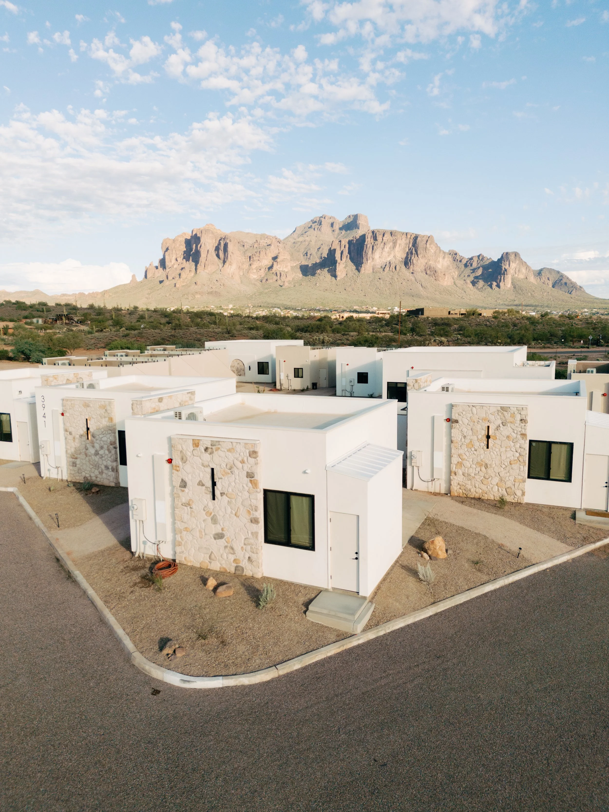 Aerial view of modern white houses with stone accents in a desert landscape with mountains in the background and a clear sky.