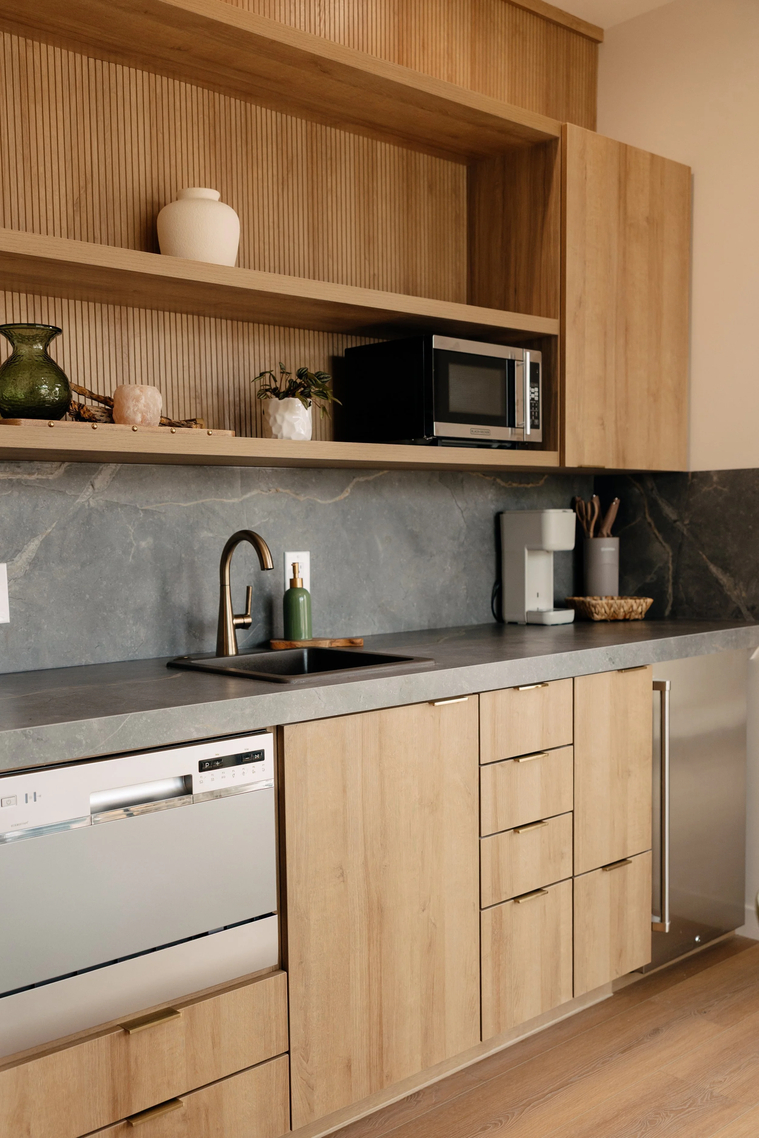 Modern kitchen with wooden cabinets, gray countertops, a microwave, a coffee maker, and decorative plants and vases.