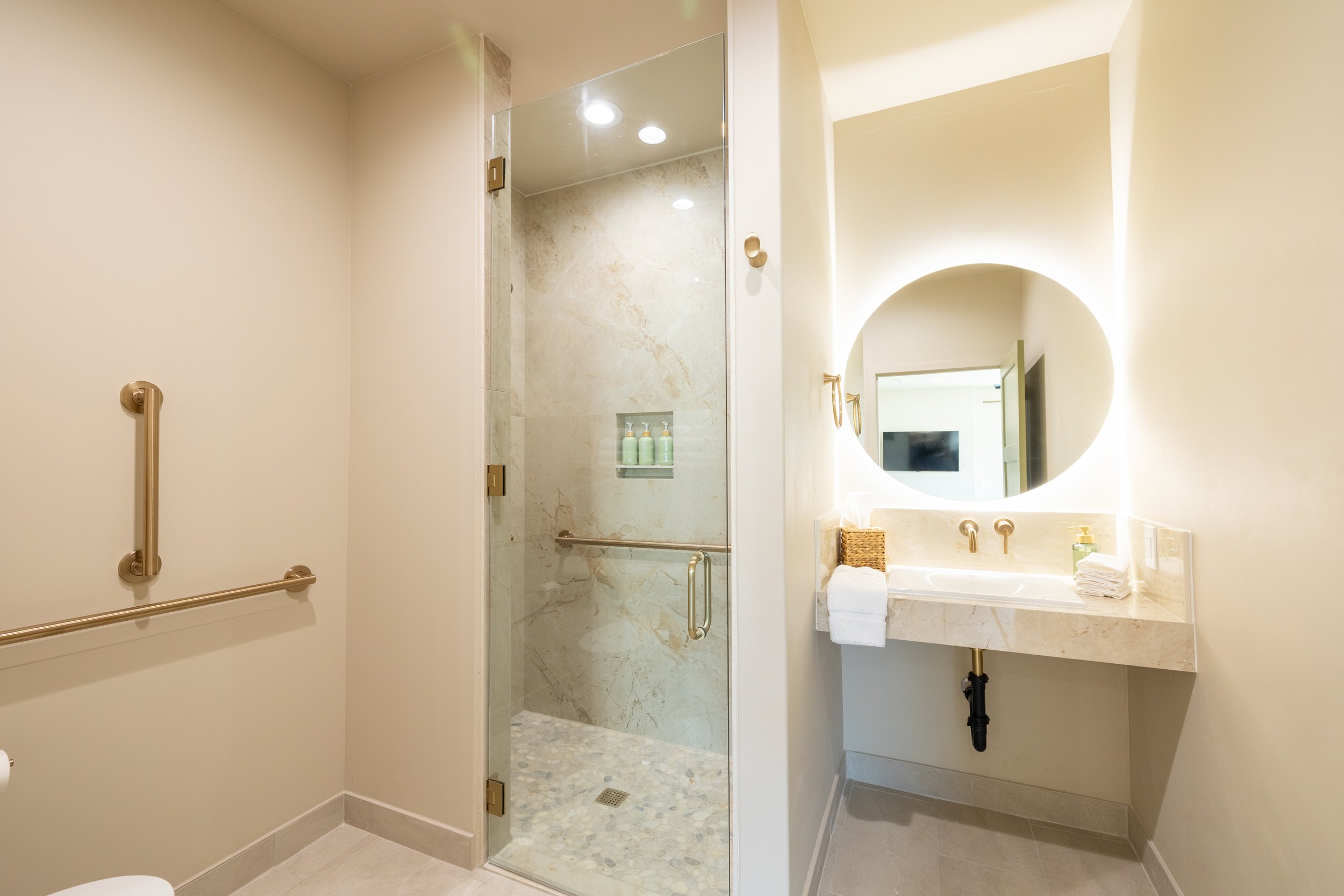 Modern bathroom with a glass enclosed shower and a vanity with a round illuminated mirror.