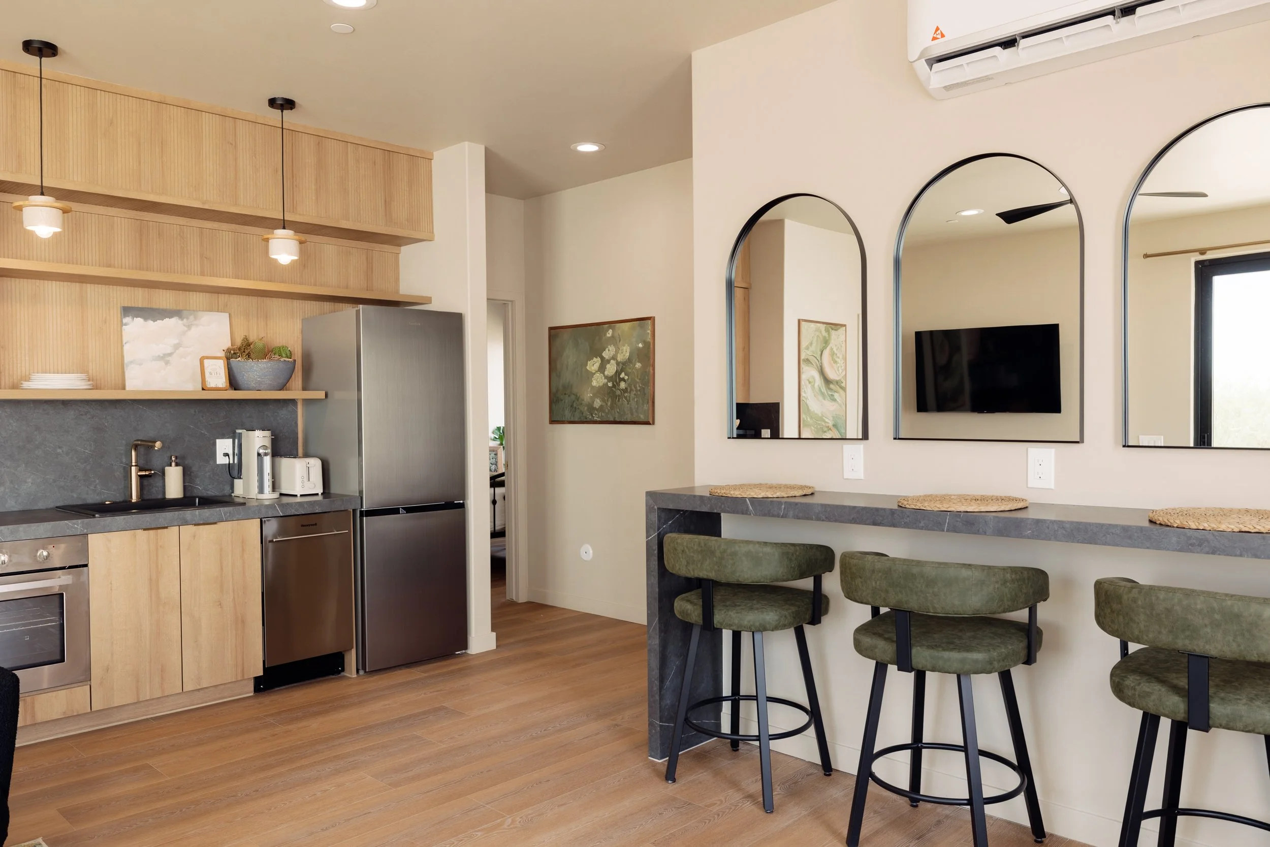 Modern kitchen with wooden cabinets, stainless steel appliances, a black countertop, and a breakfast bar with three green stools.