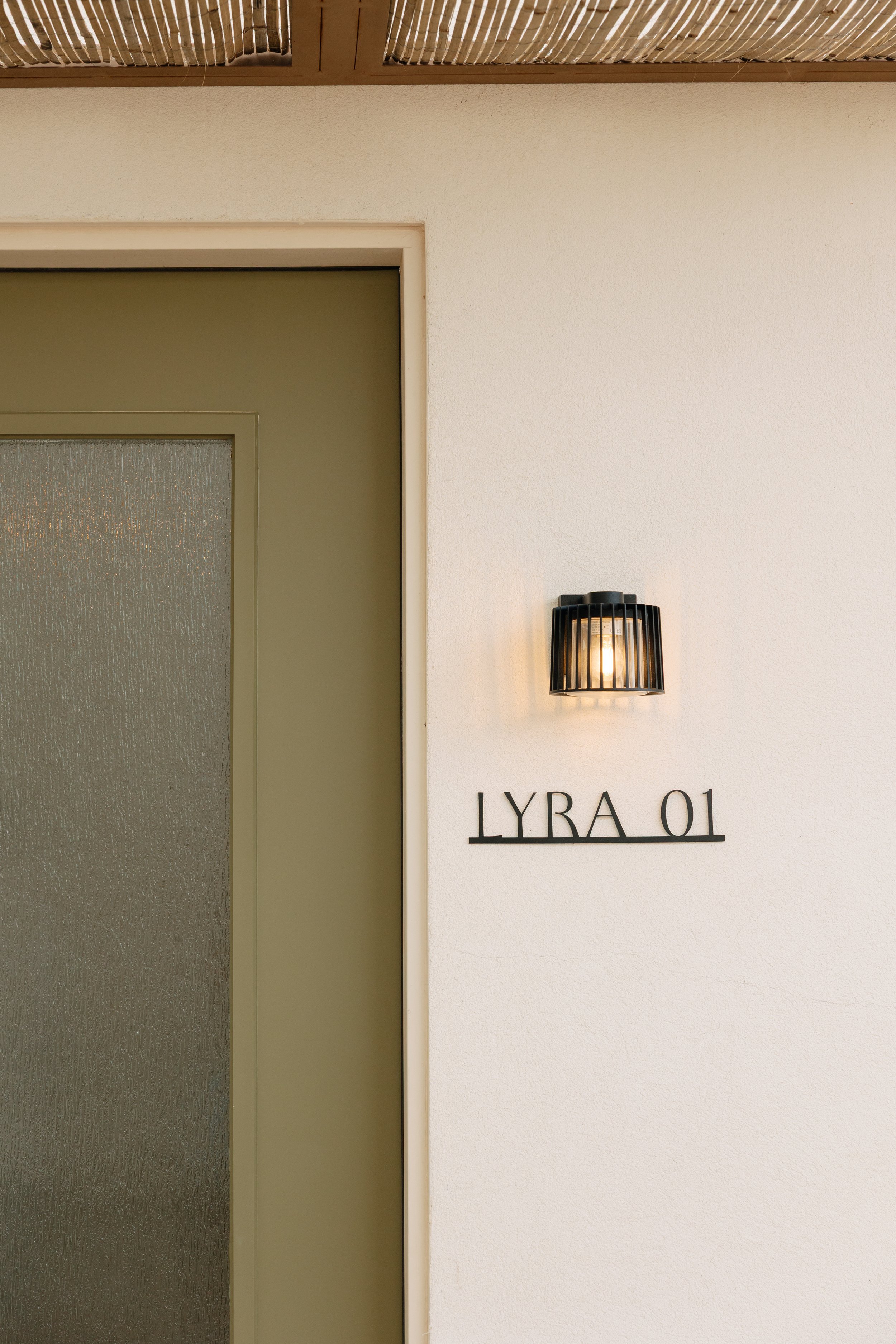 A beige wall with a black wall sconce light and the text 'LYRA 01' in black letters beside it.