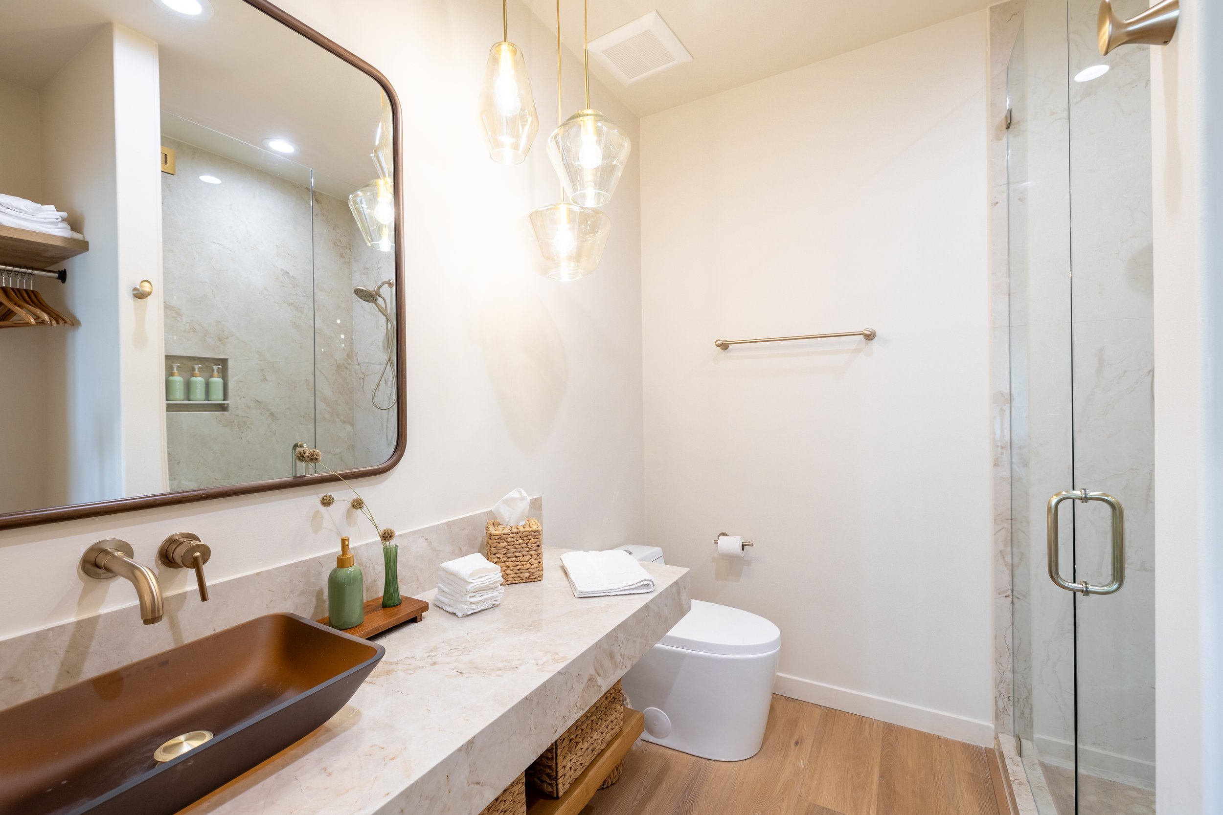 Modern bathroom with a large mirror, pendant lighting, a vessel sink, a toilet, and a glass shower door.