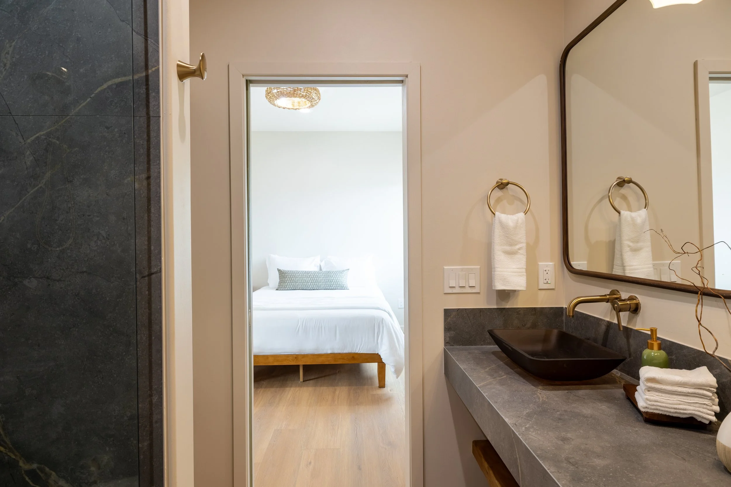 View from bathroom into a bedroom with a white bed and a chandelier ceiling light.