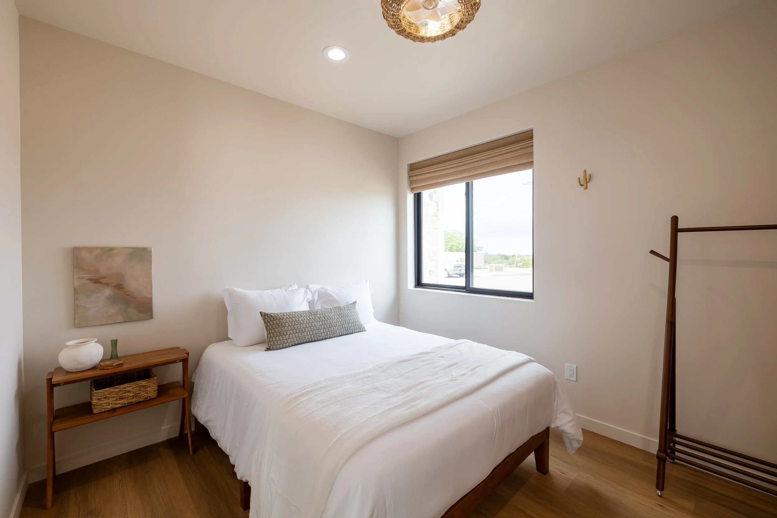 A bedroom with a bed, nightstand, window, wall decor, and a clothing rack.