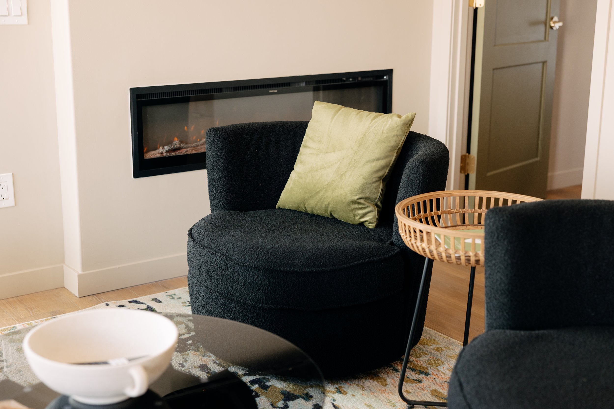 Living room with black armchair, green pillow, side table, fireplace, and partially open door