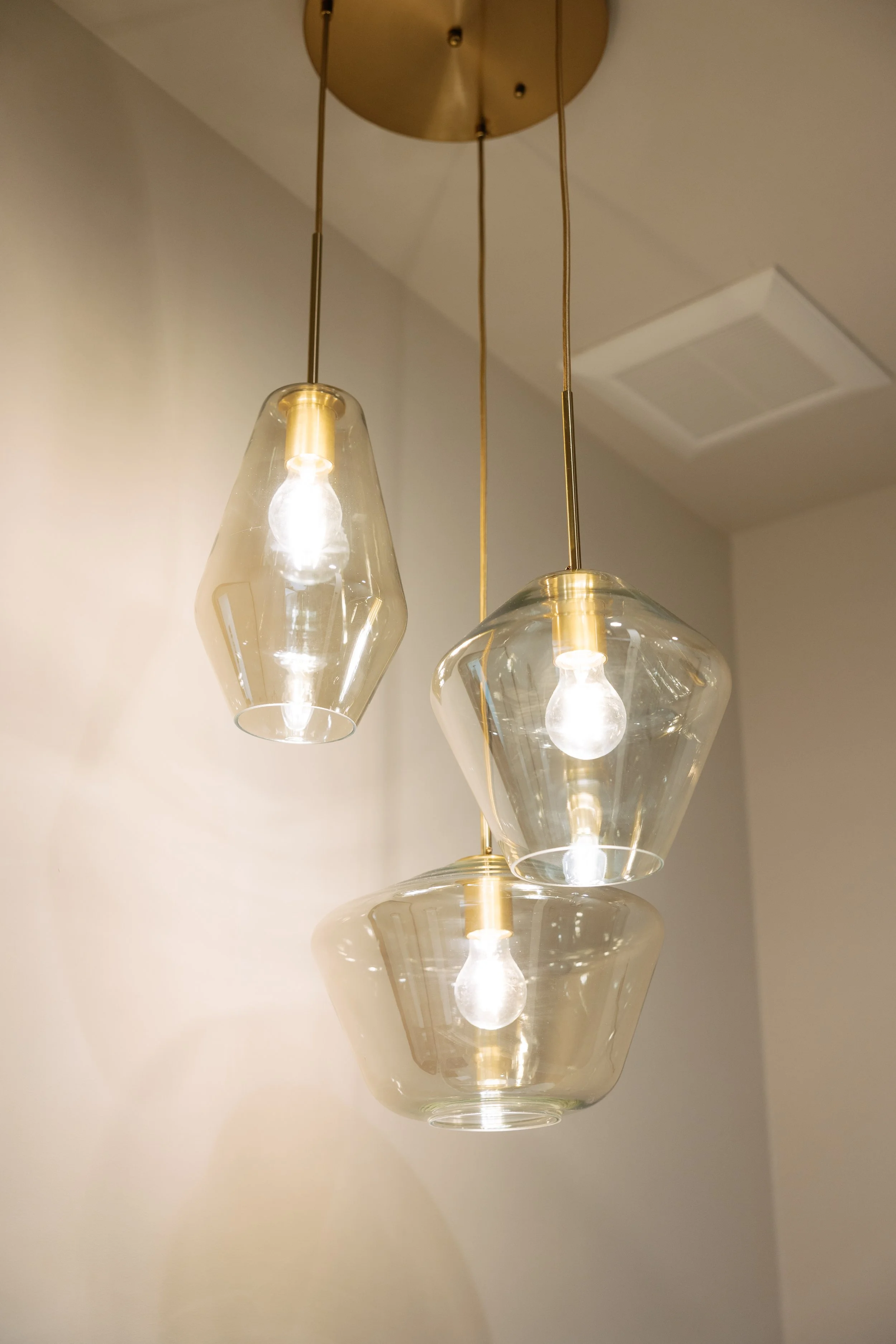 Modern hanging pendant light fixture with three glass shades and visible light bulbs, mounted on a ceiling.