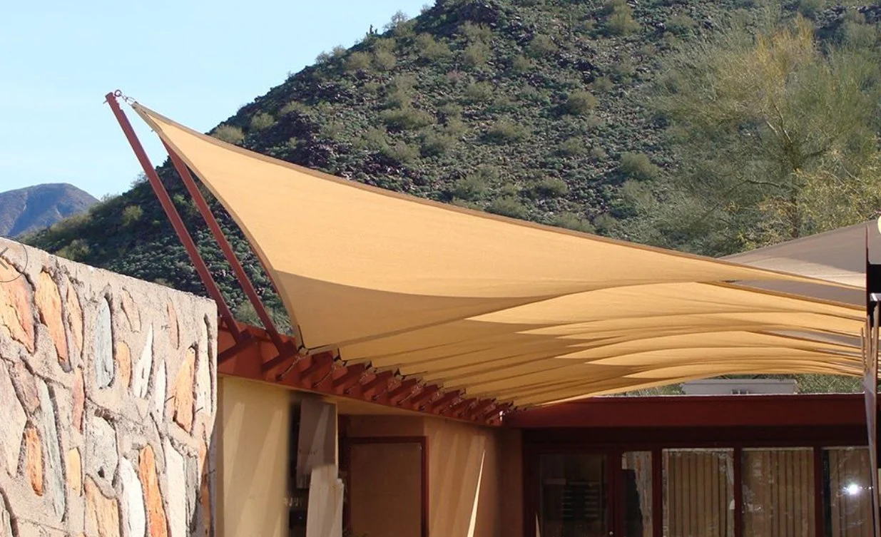Yellow fabric shade sail attached to a building, with green mountainous landscape in the background. Commercial shade sails. commercial shade awning, shade canopy, shade canopies.