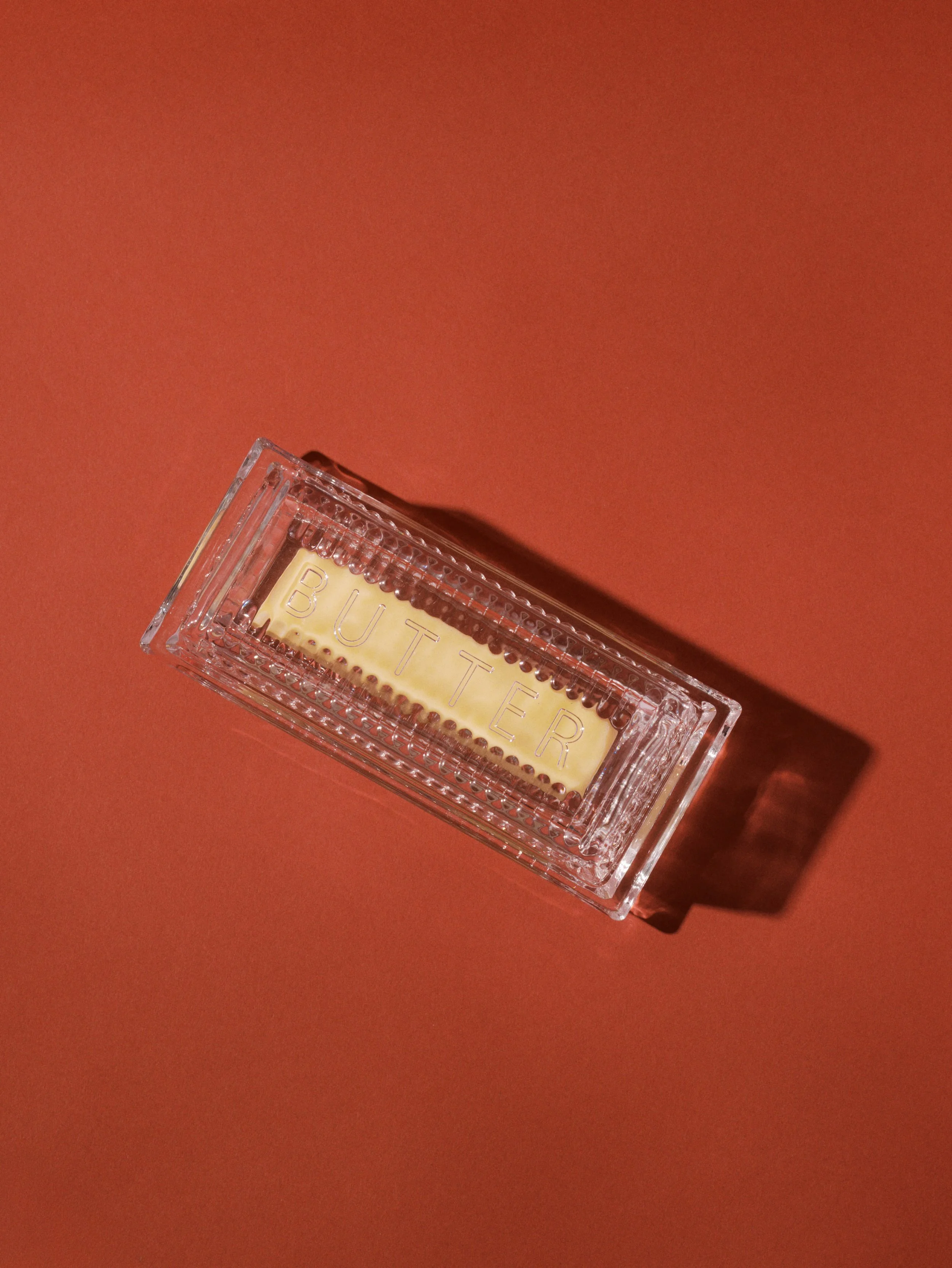 Close-up of a clear plastic container with the word 'BUTTER' engraved on it, placed on a reddish-brown surface.