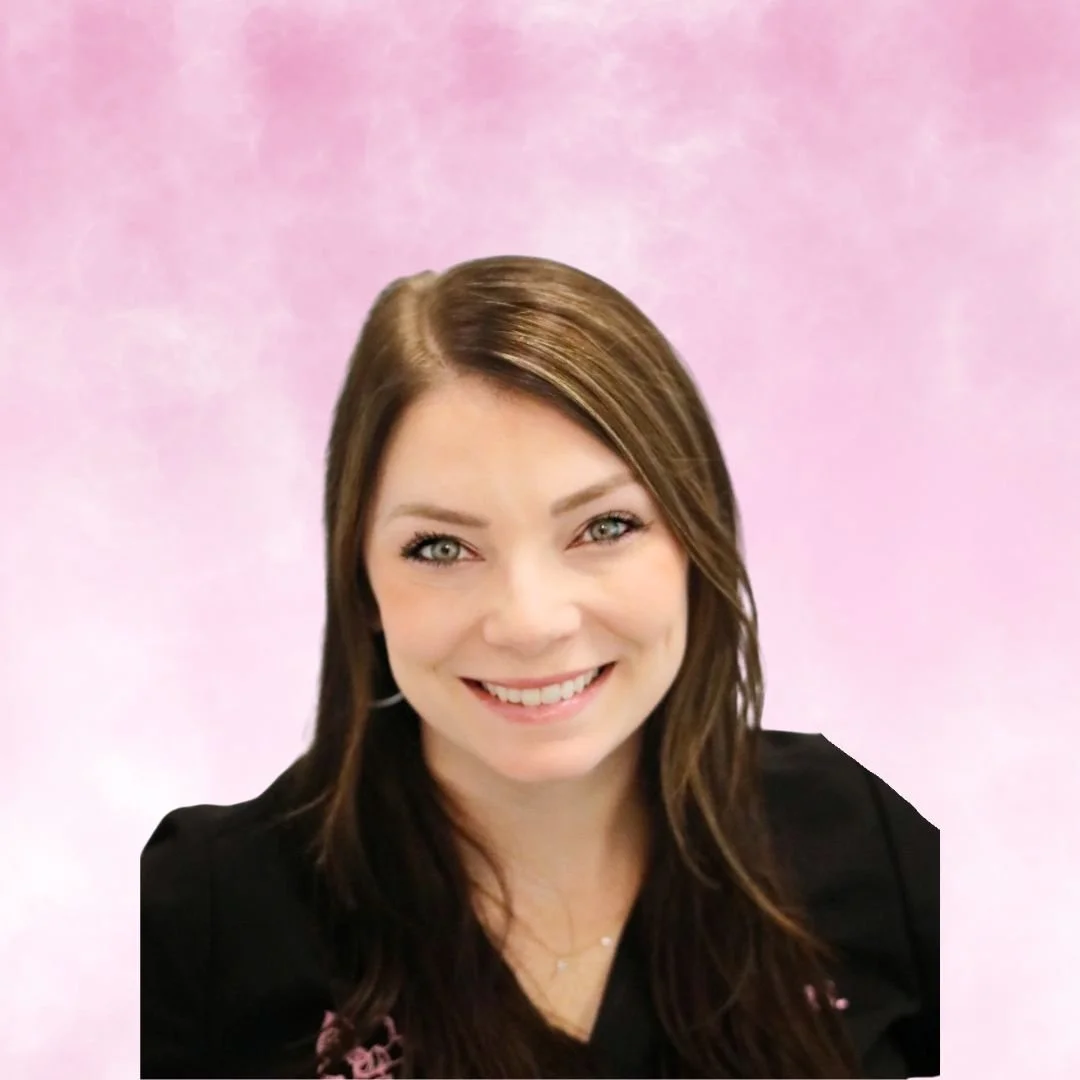 A smiling woman with brown hair and green eyes wearing a black shirt with pink embroidered text and logo, against a pink background.