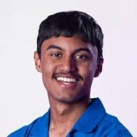 Portrait of a young man with short black hair, mustache, wearing a blue shirt, smiling against a white background.