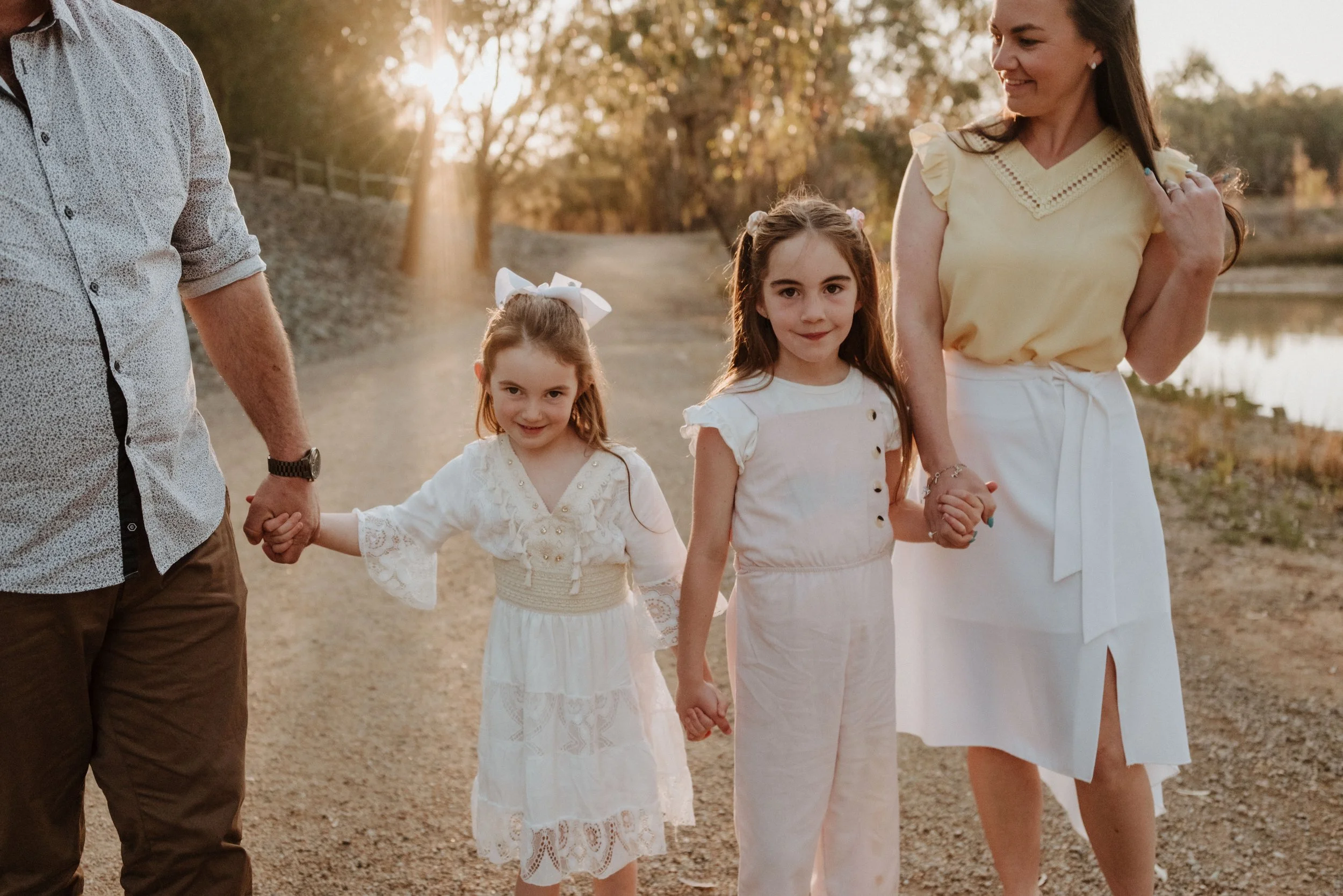 A family walking outdoors during sunset, holding hands, with lake and trees in the background.