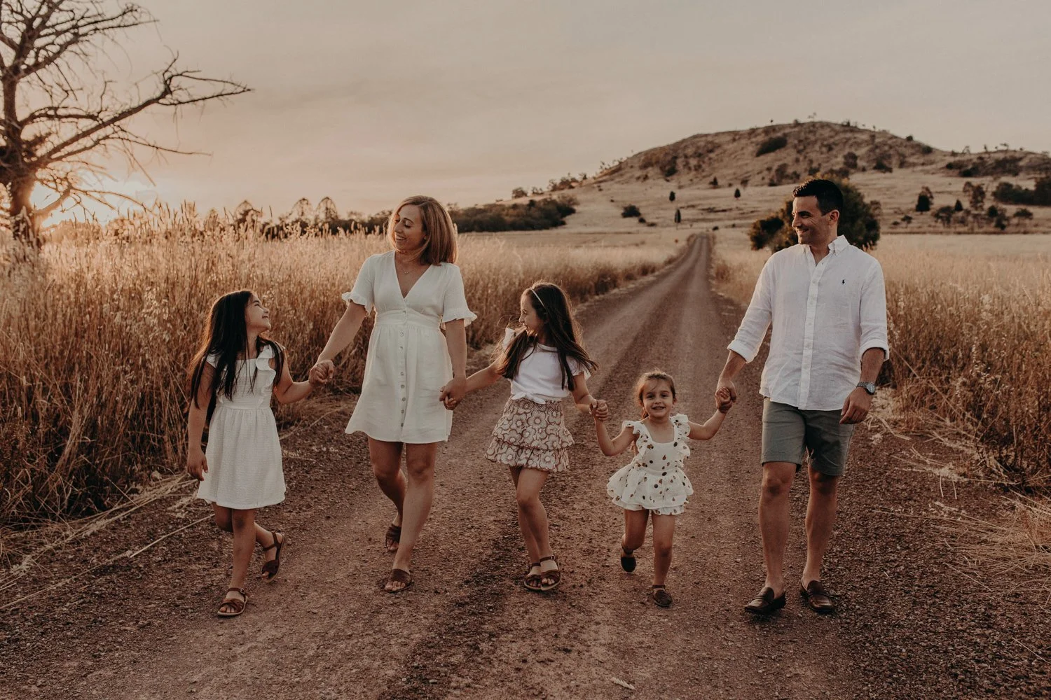 Family of six walking hand-in-hand on a dirt road through a field during sunset