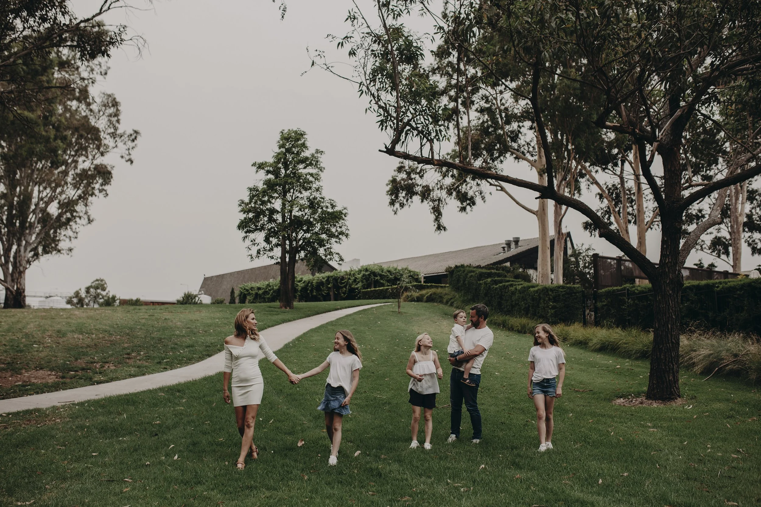 A family of six enjoying a walk in a park with green grass, walking hand in hand, under a cloudy sky.
