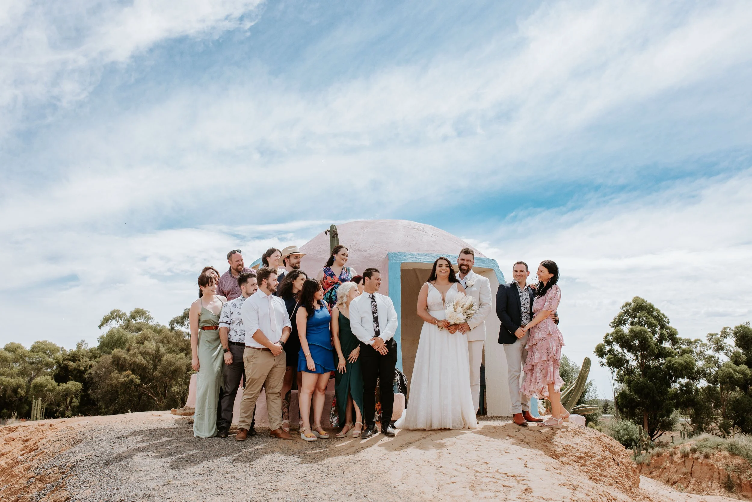 Wedding celebration with a bride and groom surrounded by family and friends outdoors in a desert landscape with clear blue sky. At Cactus Country, Strathmerton.