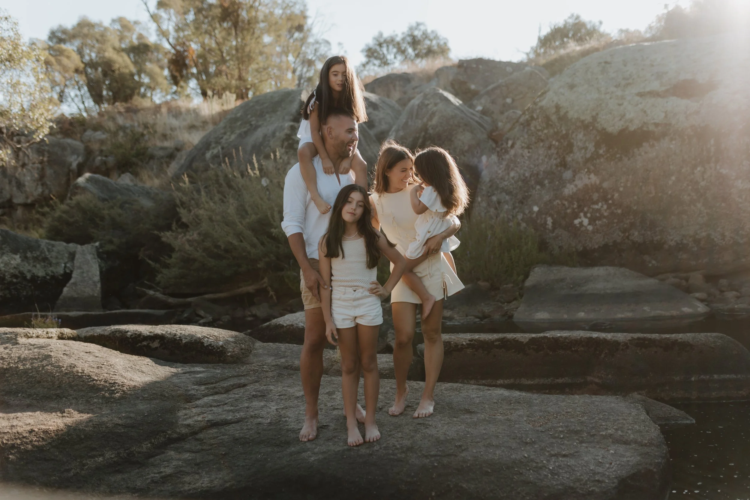 Family of five enjoying time on rocks by the water in the outdoors, sunset lighting