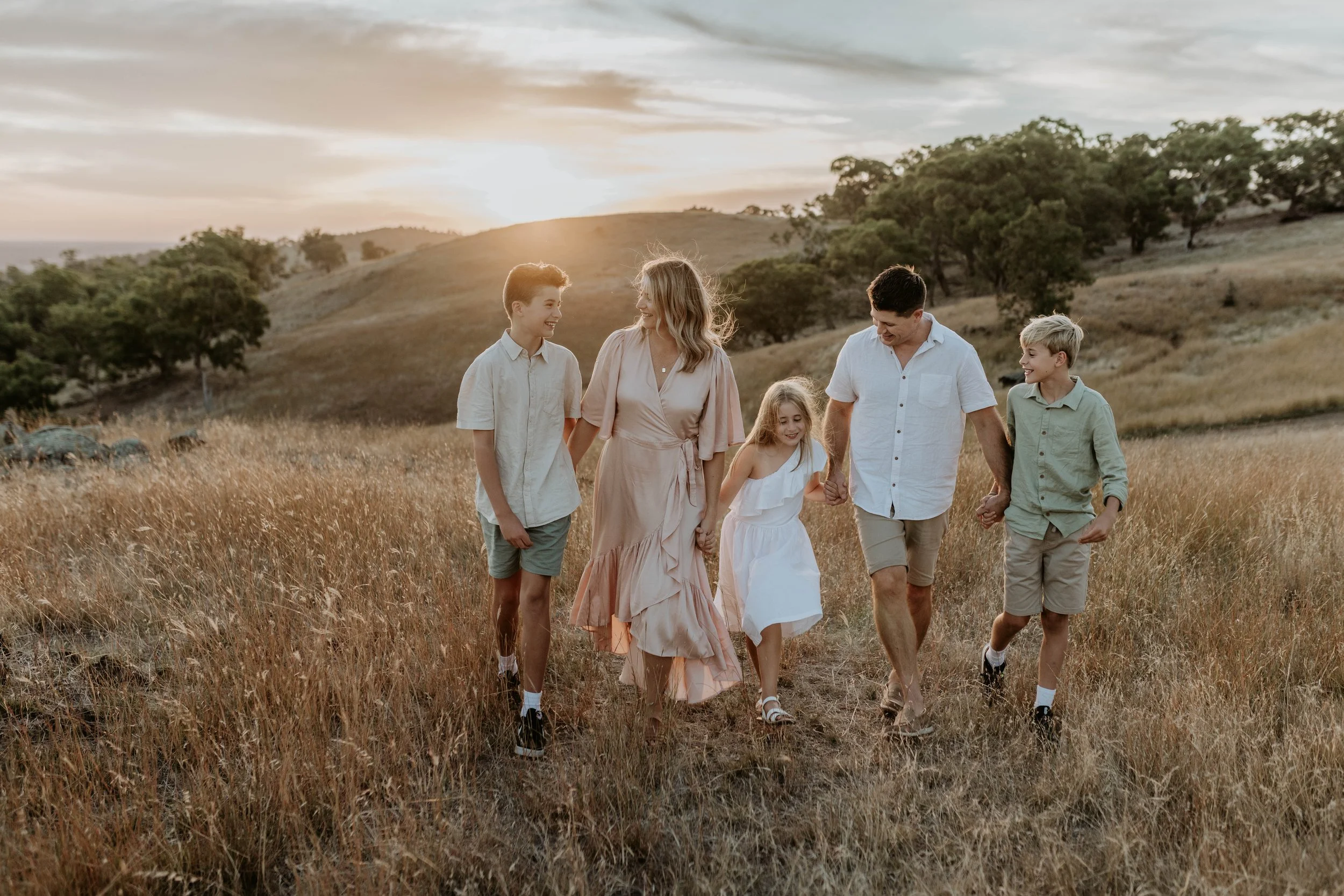 Family of six walking hand in hand through a grassy field at sunset.