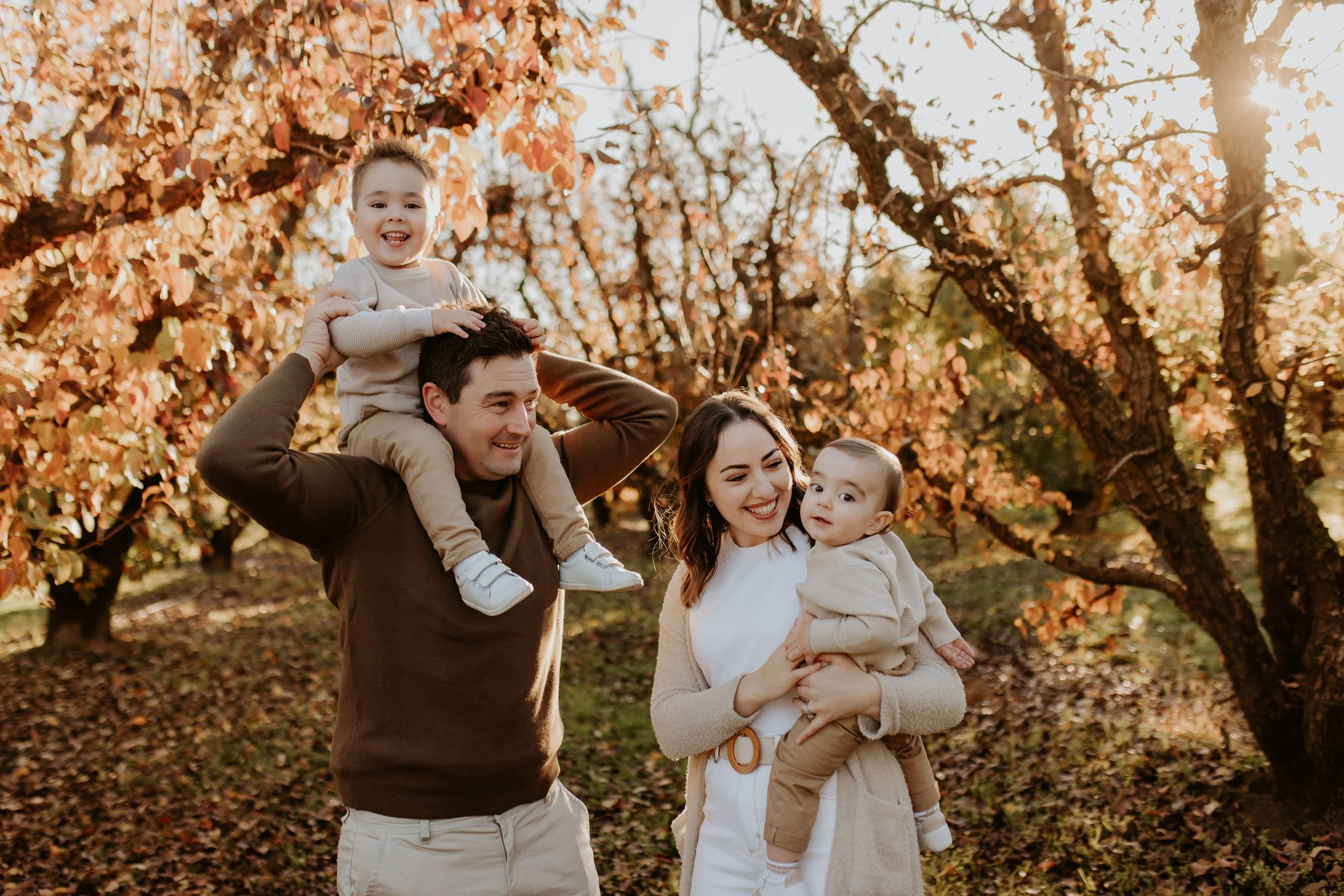 Family of four enjoying a walk outdoors during autumn, with trees with orange leaves in the background.