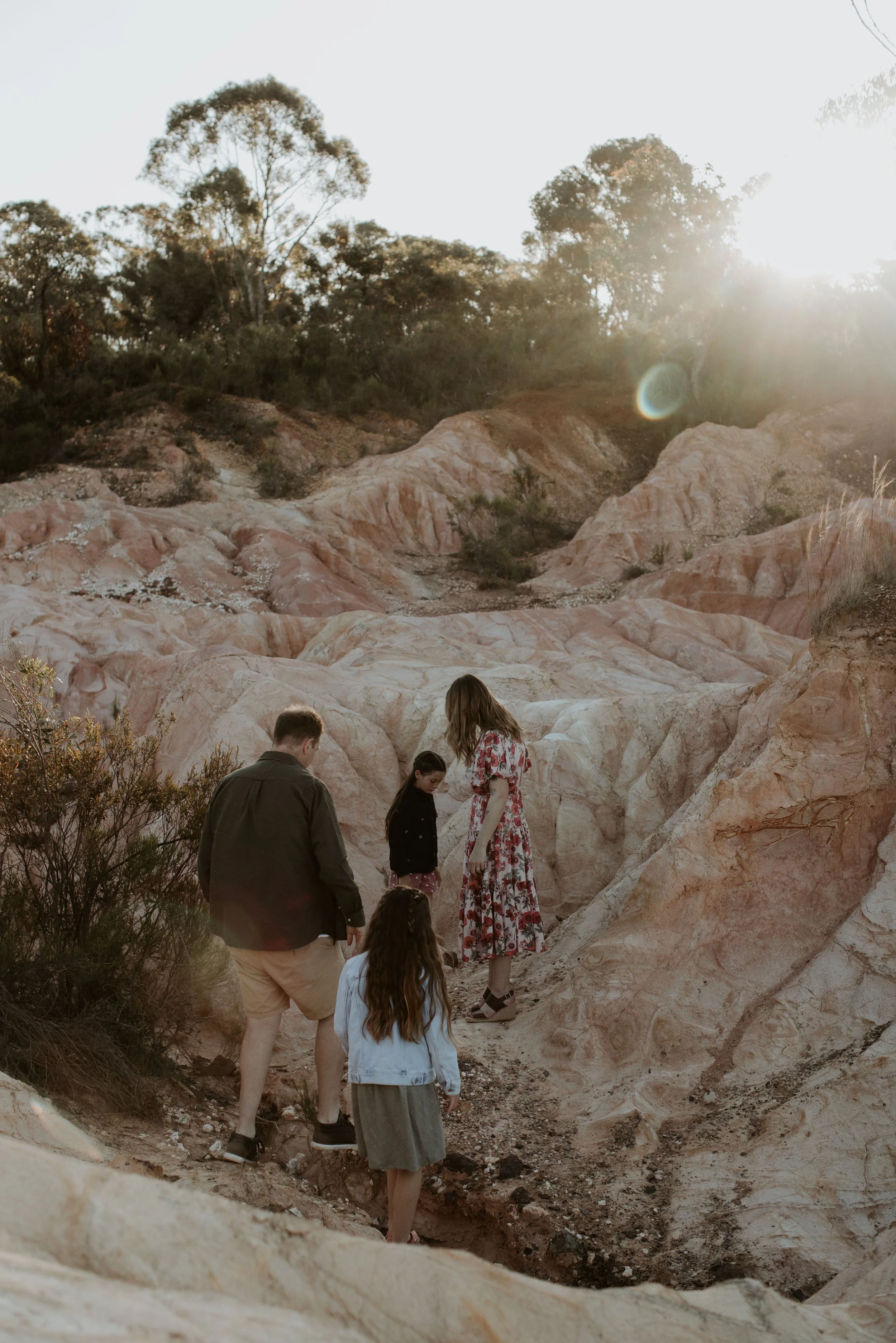 A family of five exploring rocky terrain at sunset, with a backdrop of trees and sun glare.