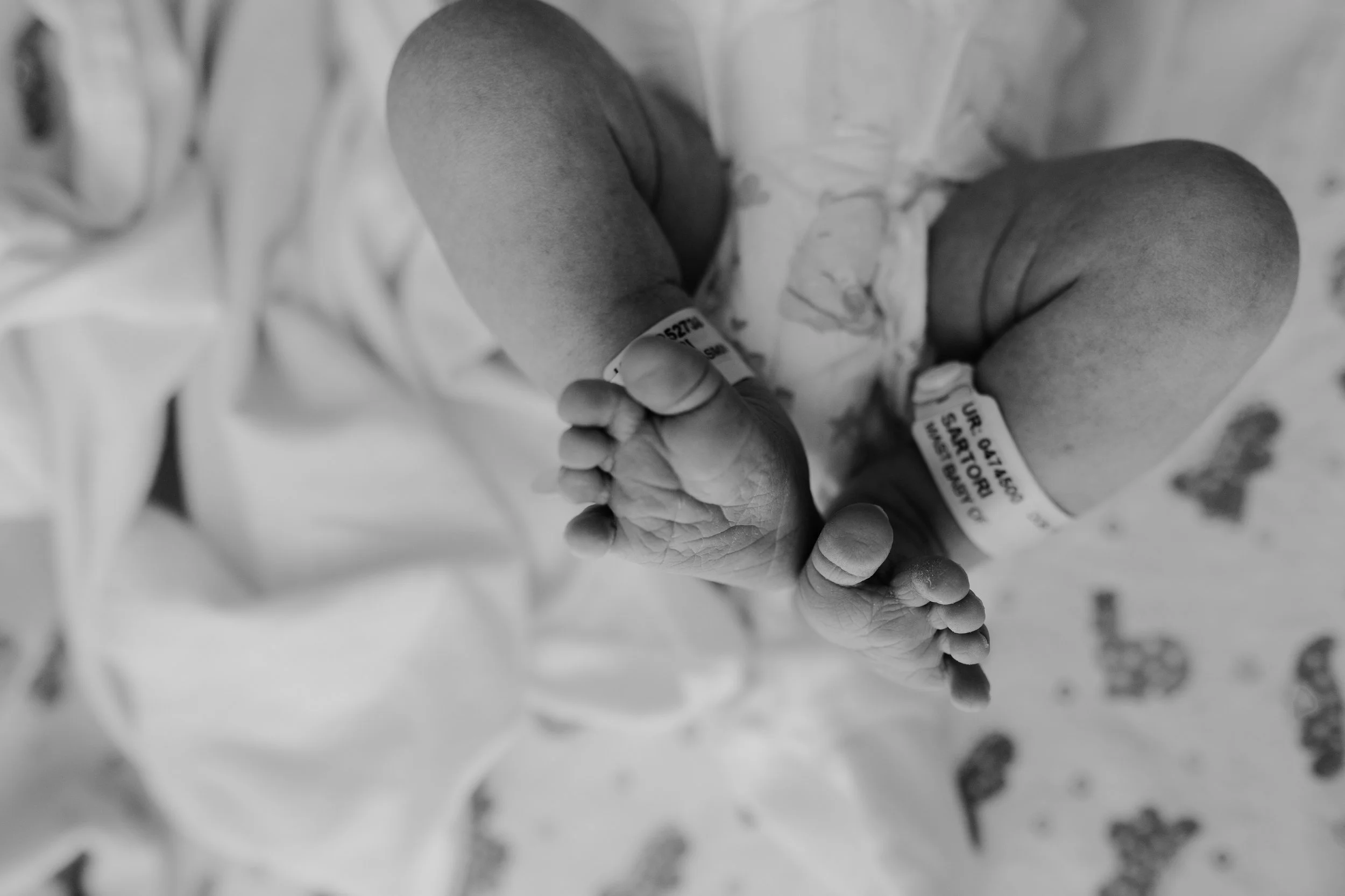 Black and white photo of a newborn baby in a hospital, lying on a hospital bed, with wristbands on both wrists.