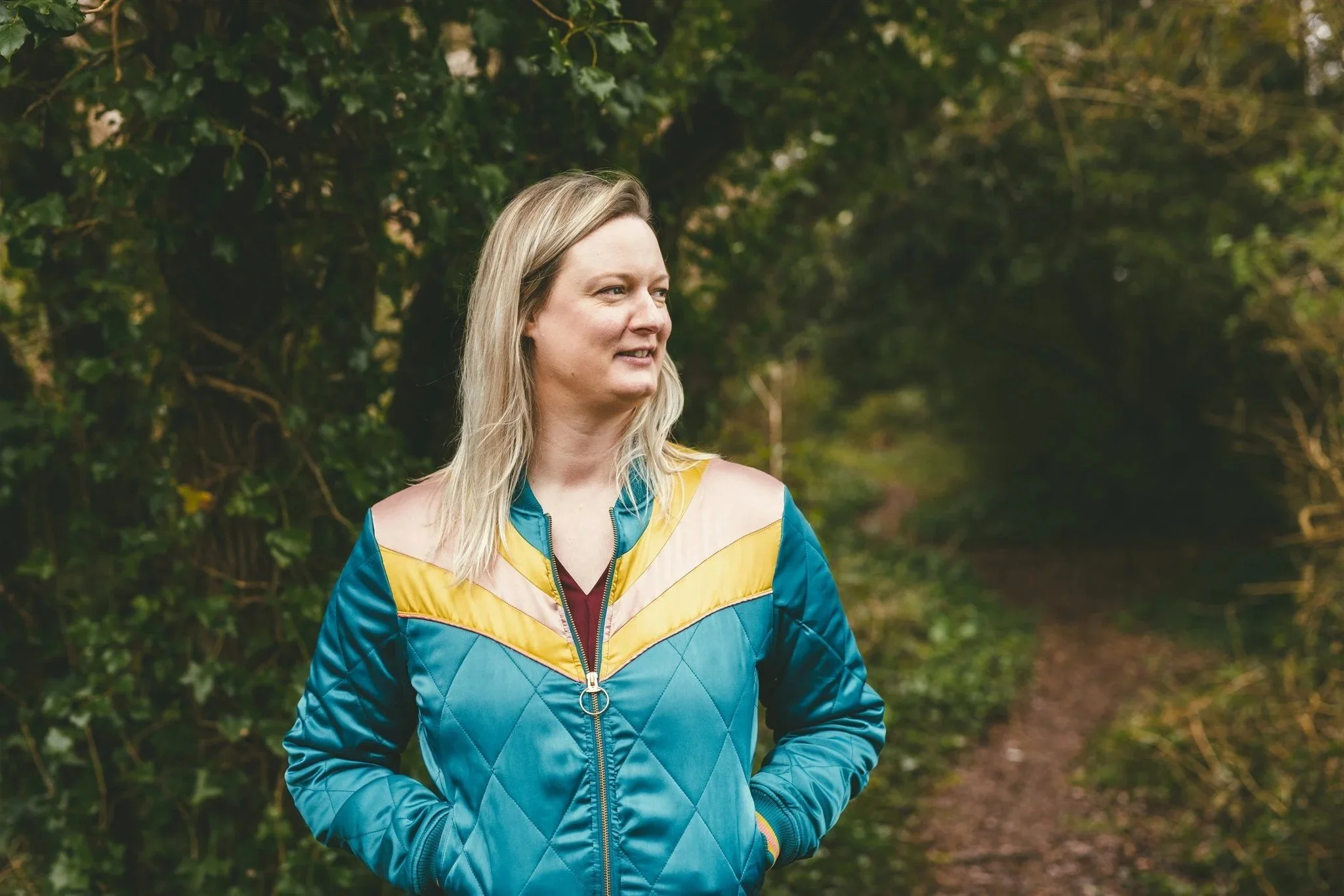 Cath Harris MBA is a white woman with light hair and wears a brightly coloured jacket. She is looking to the right and slightly smiling