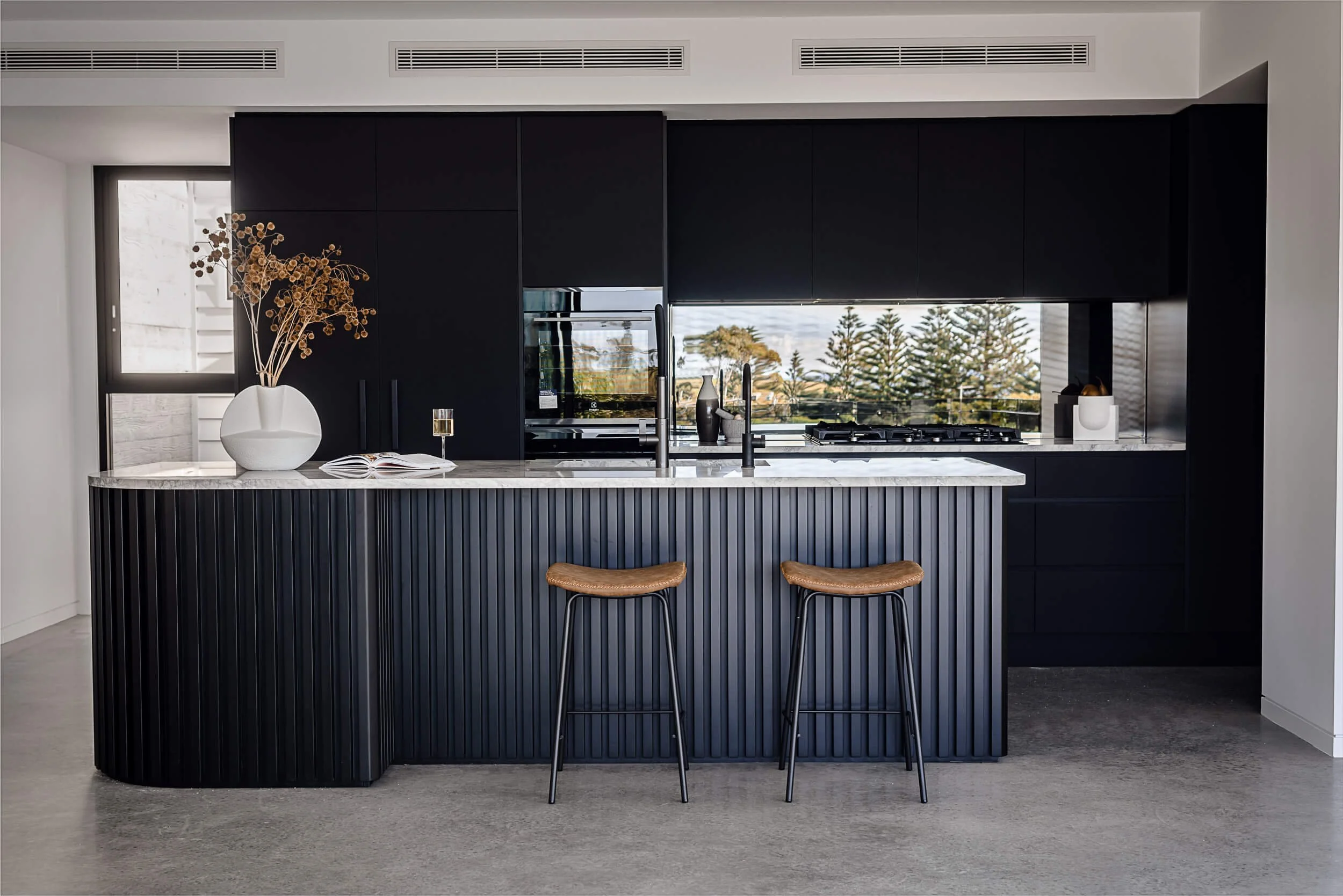 Premium architectural photography and film documenting true materiality and craftsmanship—highlighting ribbed kitchen island profiles, dark matte cabinetry, and polished concrete floors—for Master Builders and designers in Regional NSW.