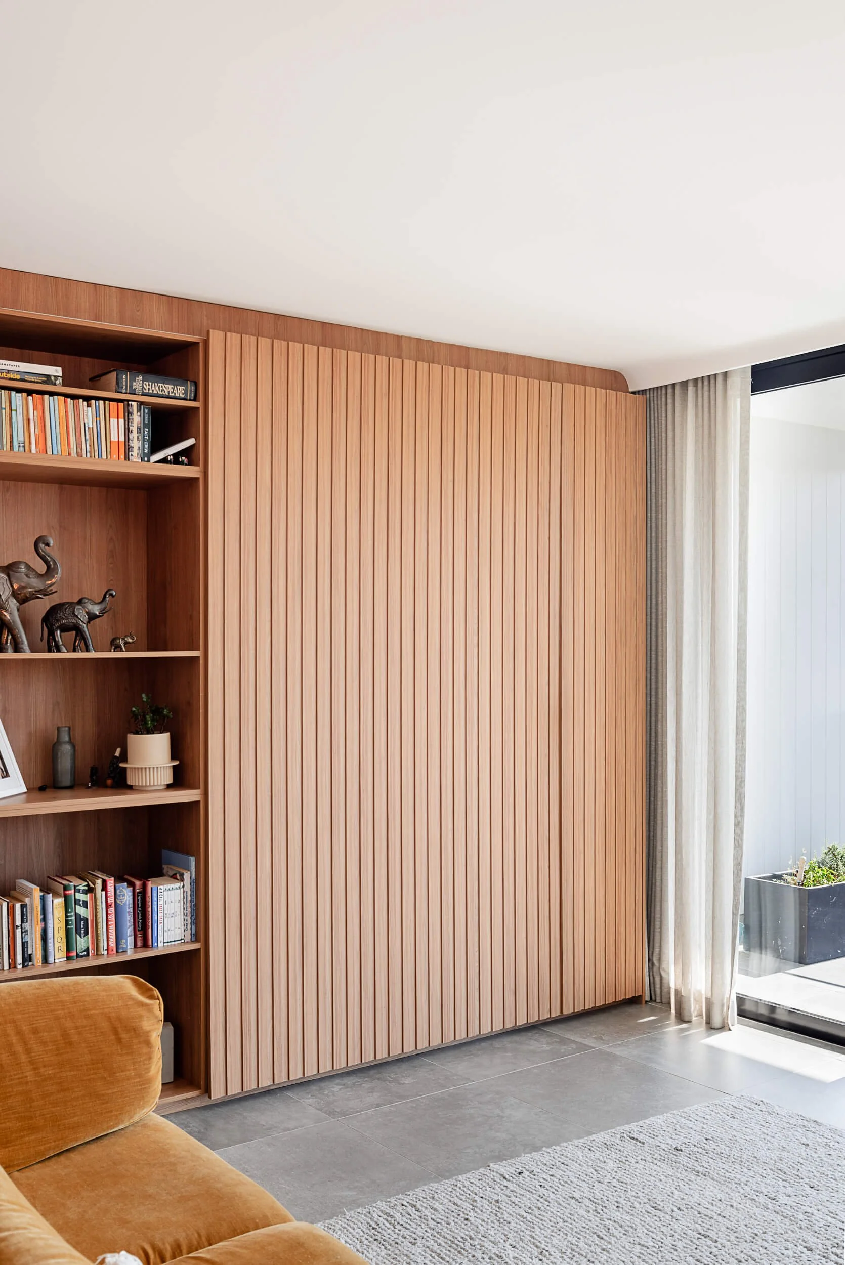 Custom timber bookcase shelving and floor-to-ceiling timber batten feature wall alongside a velvet sofa at Bondi Heights in Sydney, NSW