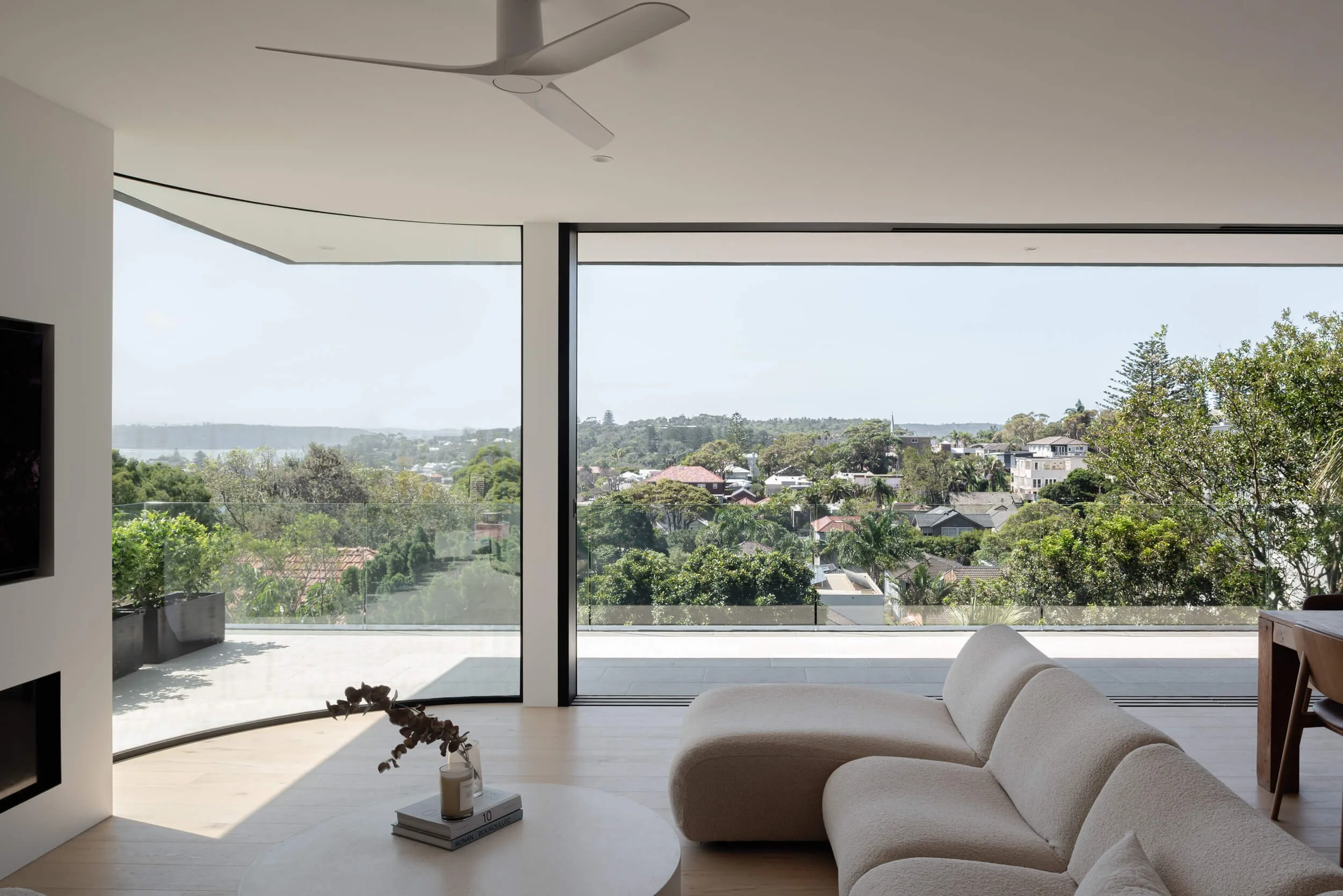 Open living space with curved glass window facing coastal backdrop at Stonemasons House in Vaucluse, NSW