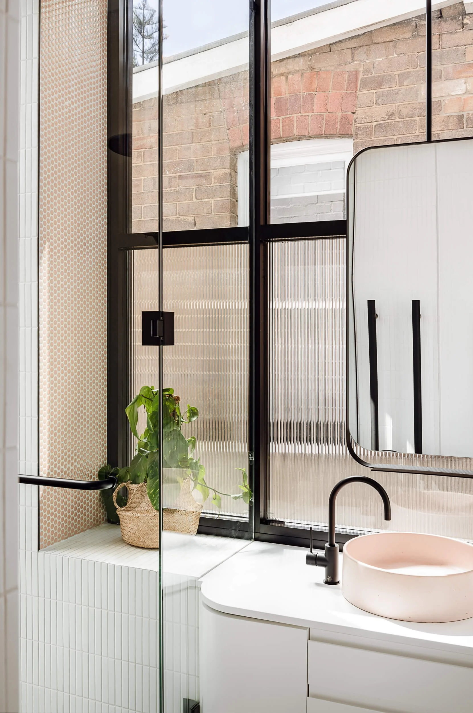 Curved white bathroom vanity featuring a blush pink concrete basin, matte black tapware, and a fluted glass window at Bondi Heights in Sydney, NSW