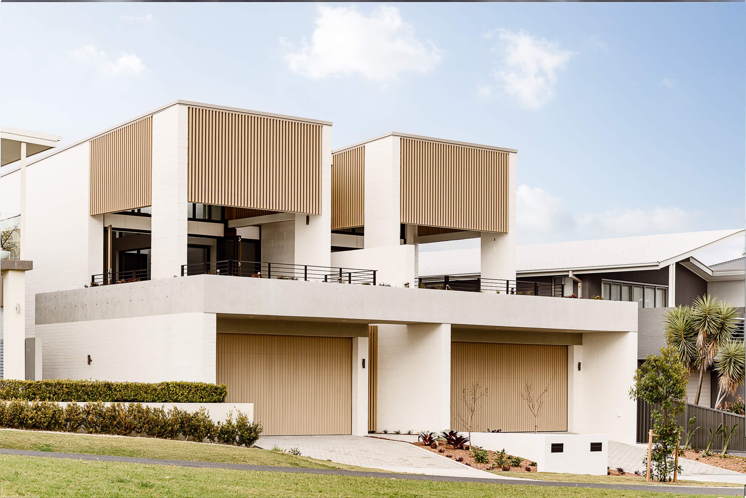 O'Brien Duplex coastal exterior in Bulli NSW featuring timber batten screens, painted brick structure, and garage entry by SLD Projects and Kibbin Design