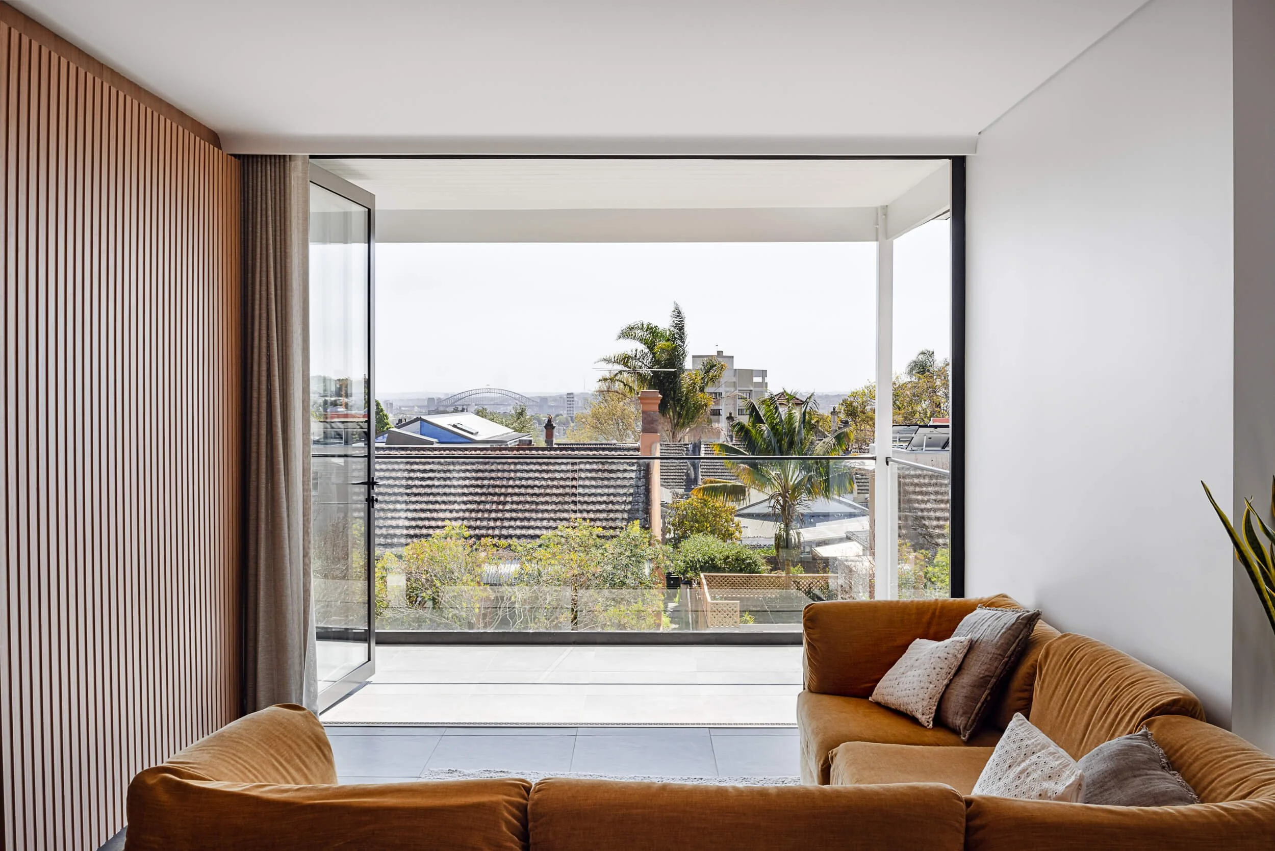 Upper living room featuring a timber slat feature wall and open sliding glass doors leading to a balcony with Harbour Bridge views at Bondi Heights in Sydney, NSW