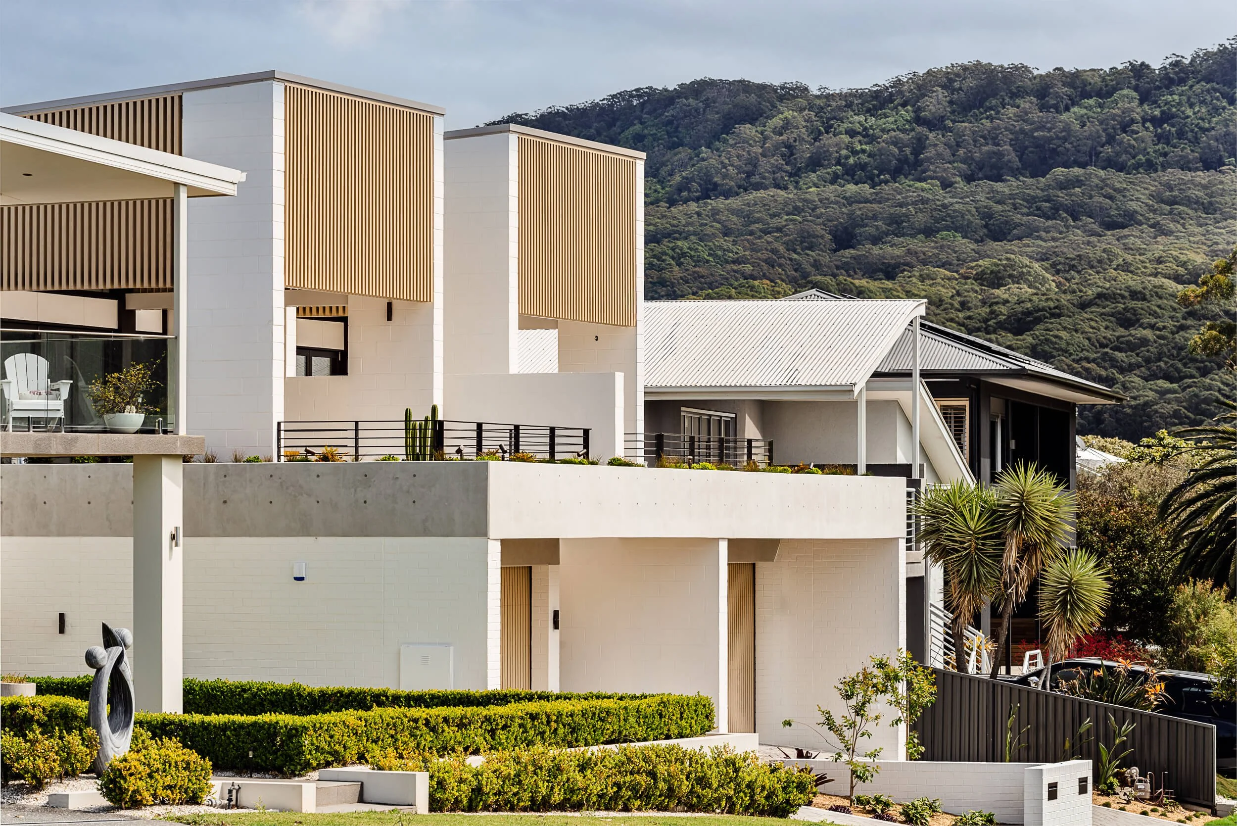 O'Brien Duplex exterior in Bulli framed against the Illawarra escarpment, showcasing painted brick, timber batten screens, and concrete terrace by SLD Projects and Kibbin Design