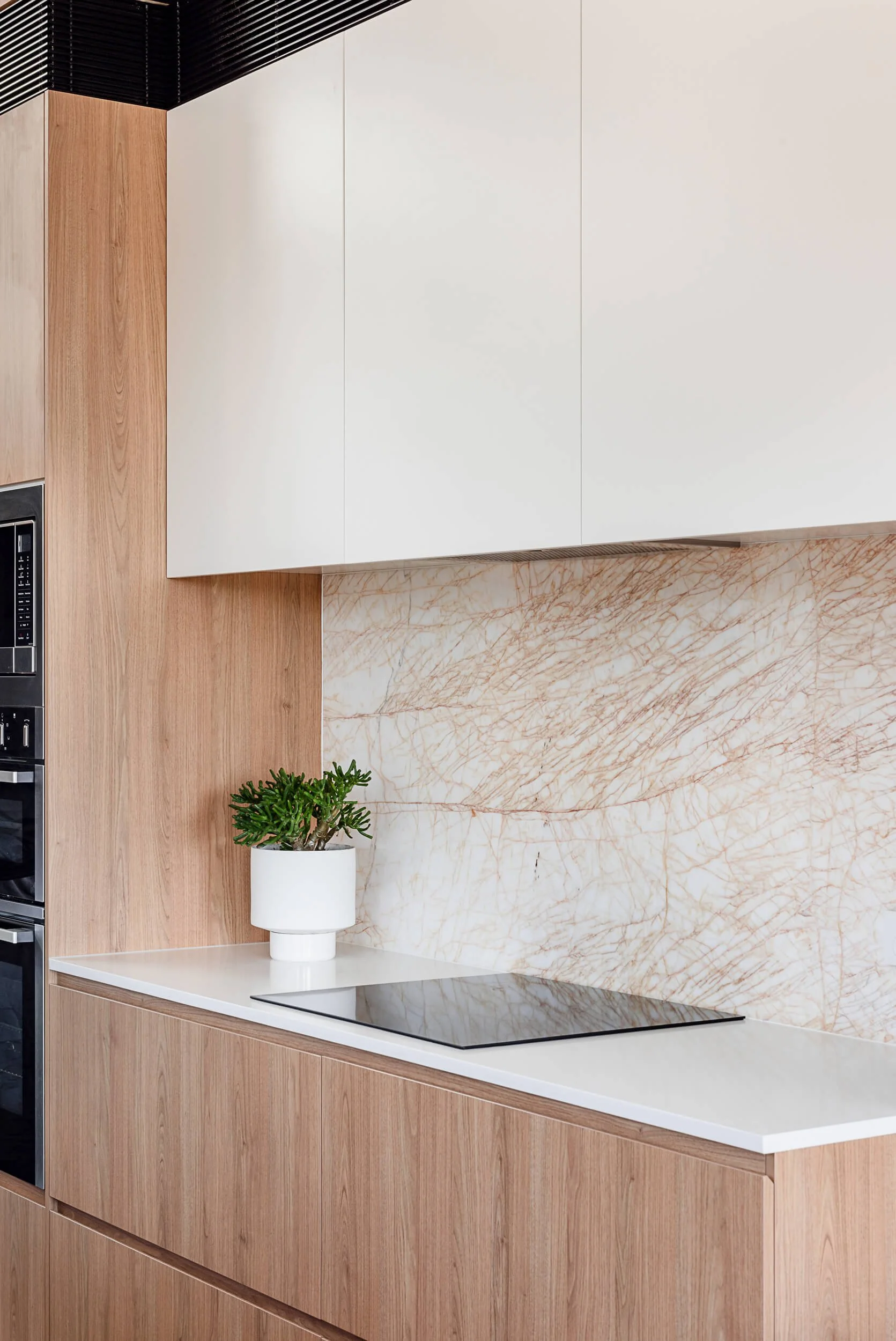 Detailed view of light oak kitchen joinery, matte white upper cabinets, and a veined marble splashback behind an induction cooktop at Bondi Heights in Sydney, NSW