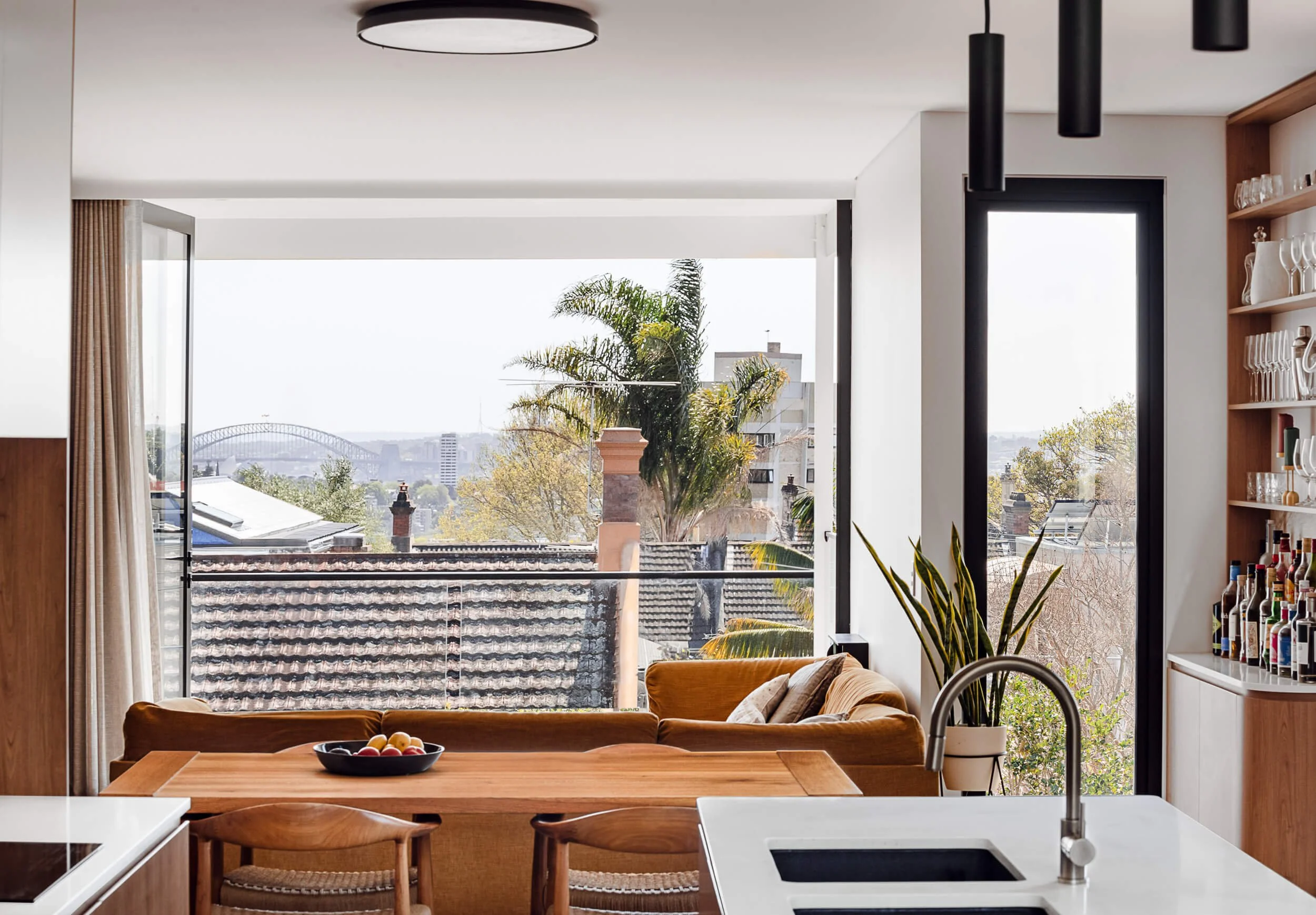 Upper-level open-plan kitchen and dining area with a warm modular sofa framing sweeping views of the Sydney Harbour Bridge at Bondi Heights in Sydney, NSW
